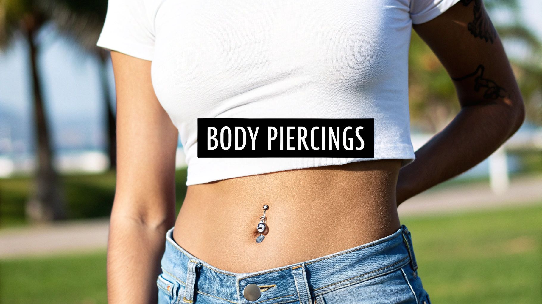 A person's midsection wearing a white crop top and jeans, showing a decorative belly button piercing.