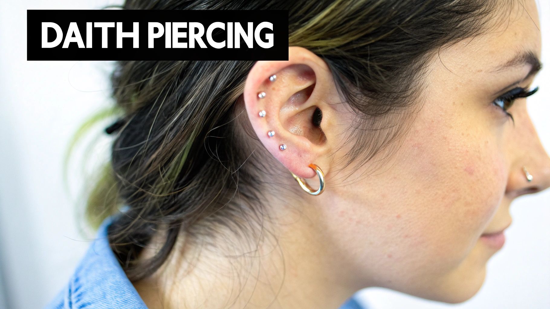 Close-up of an ear with multiple stud piercings, a gold hoop, and text "DAITH PIERCING".