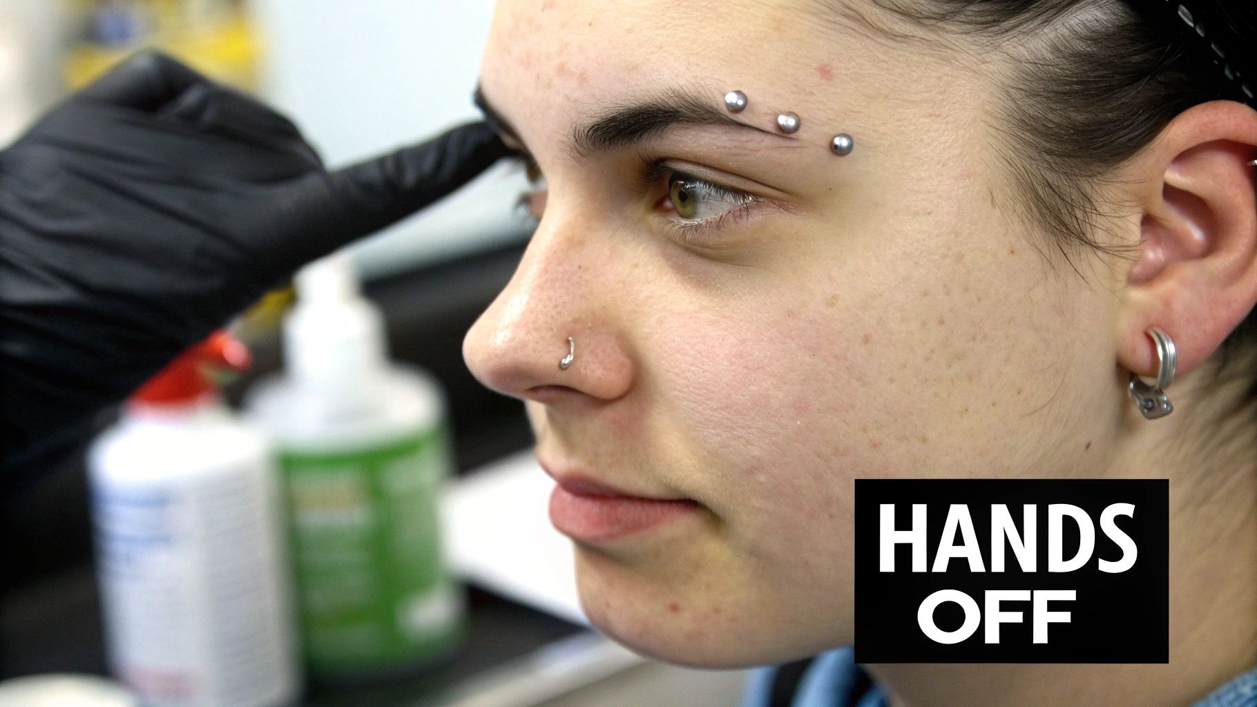 Close-up of a person's face with three new eyebrow piercings and a nose ring.