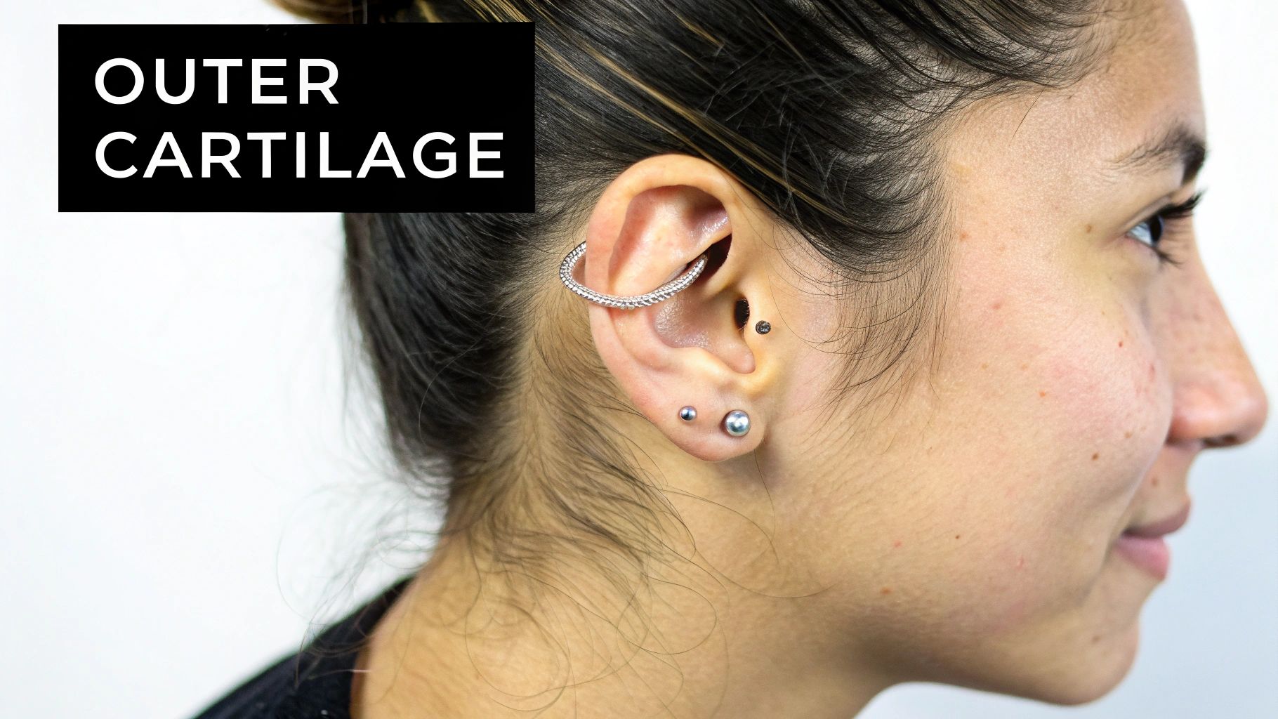 Close-up of a woman's ear featuring an outer cartilage piercing with a silver hoop, a helix, and two lobe piercings.