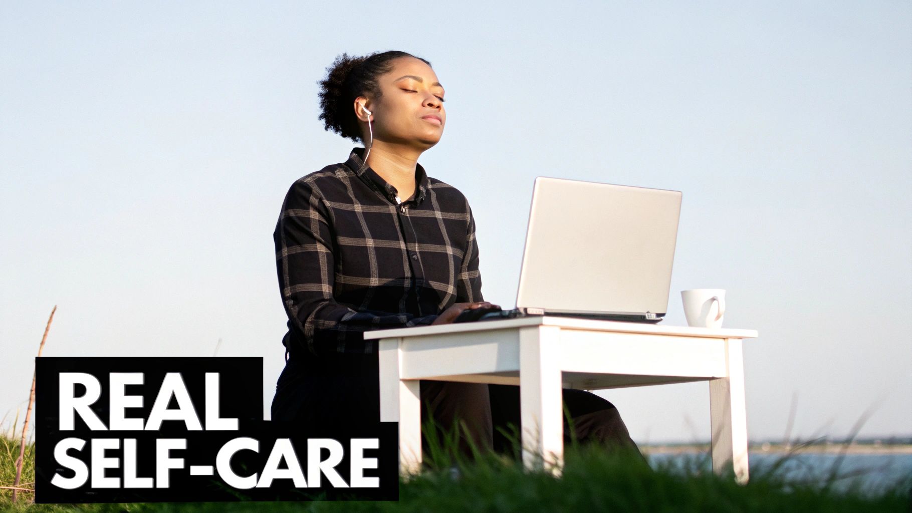 A young woman meditates outdoors with her laptop and earbuds, practicing real self-care.