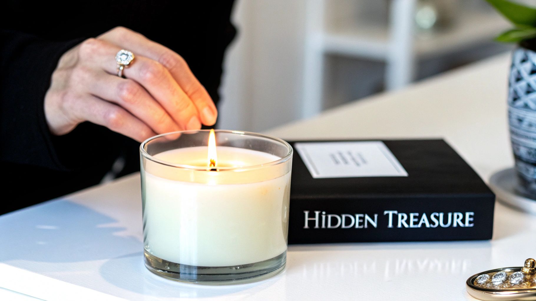 A person's hand with a ring reaches for a lit candle next to a "Hidden Treasure" box.