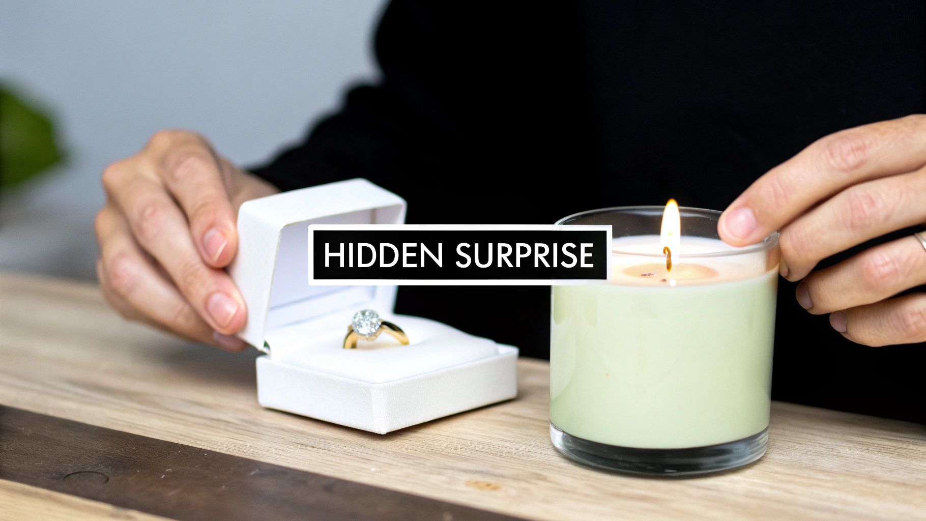 Hands opening a white ring box revealing a sparkling diamond engagement ring next to a lit candle.