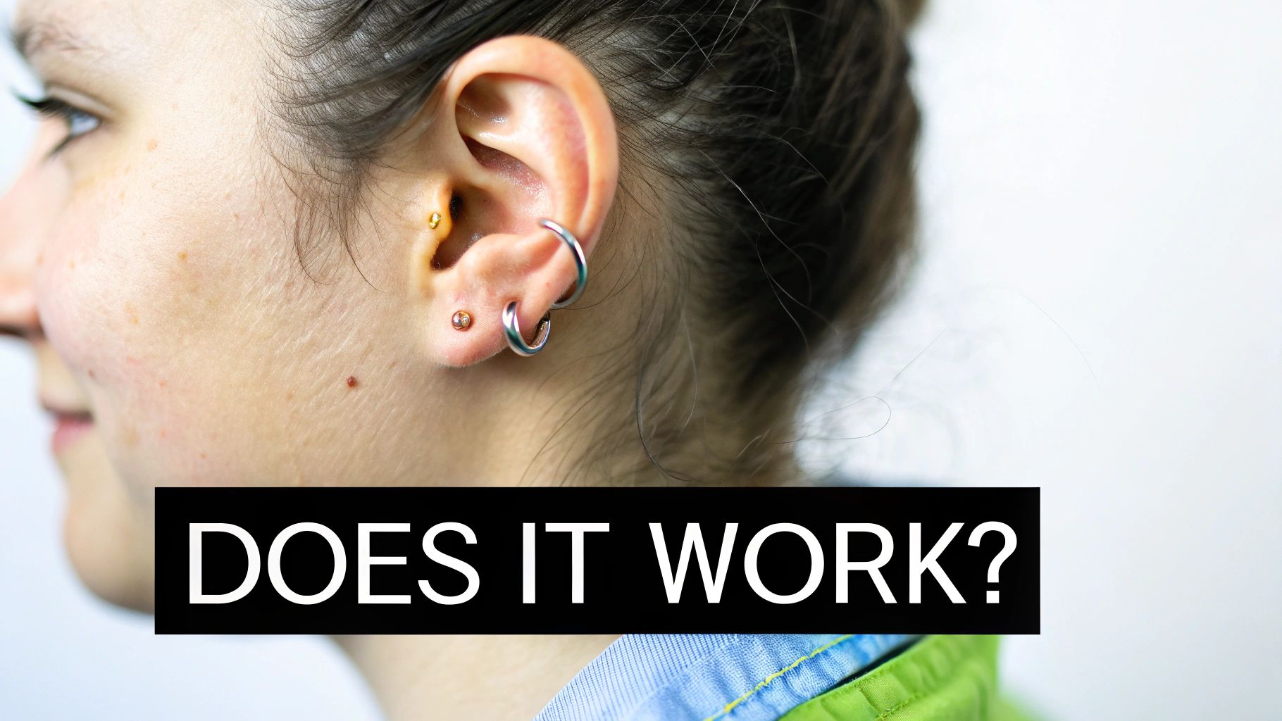 Close-up of a person's ear with a gold daith piercing and multiple silver hoop earrings.