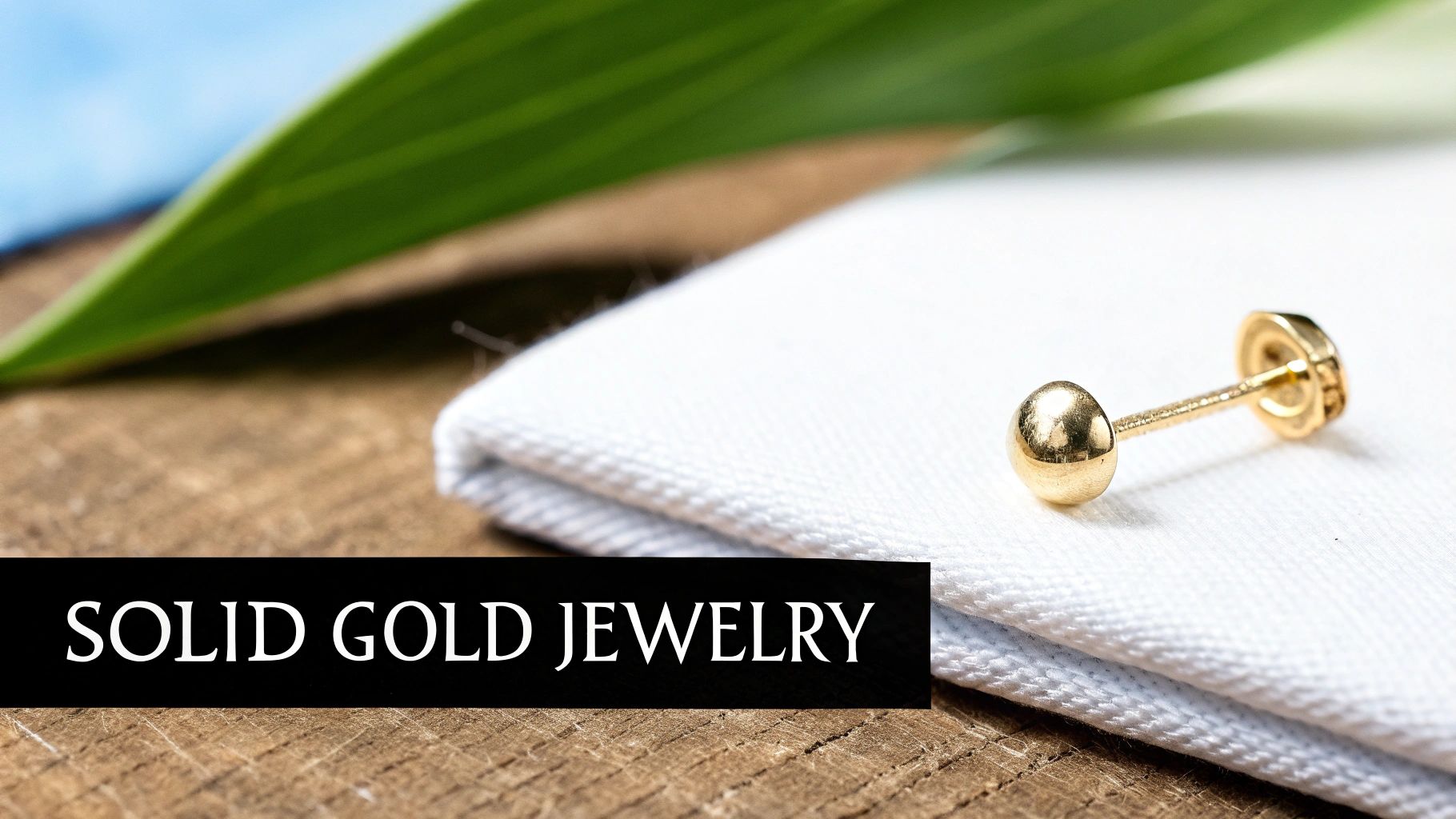 A single solid gold stud earring on white fabric, with a blurred green leaf and blue sky background, and text "SOLID GOLD JEWELRY".
