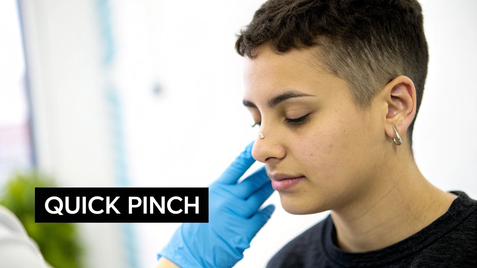 A person with a nose piercing has their nose gently touched by a gloved hand, eyes closed.