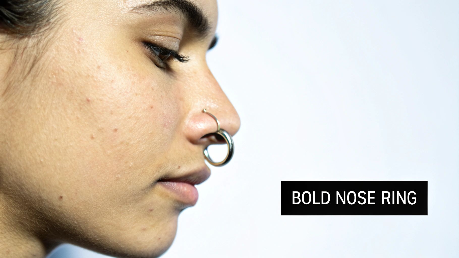 A close-up profile view of a person wearing a bold silver nose ring on a white background.