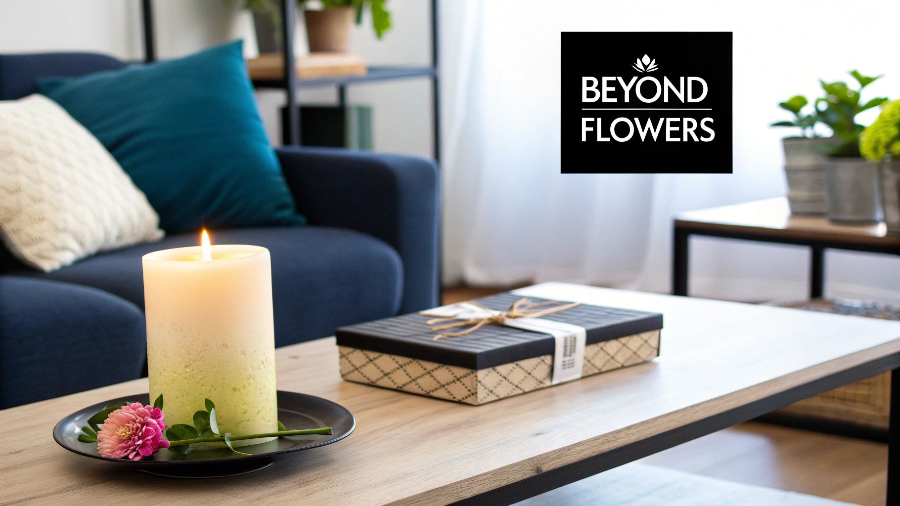 A lit candle with a pink flower and a decorative gift box sit on a wooden coffee table.