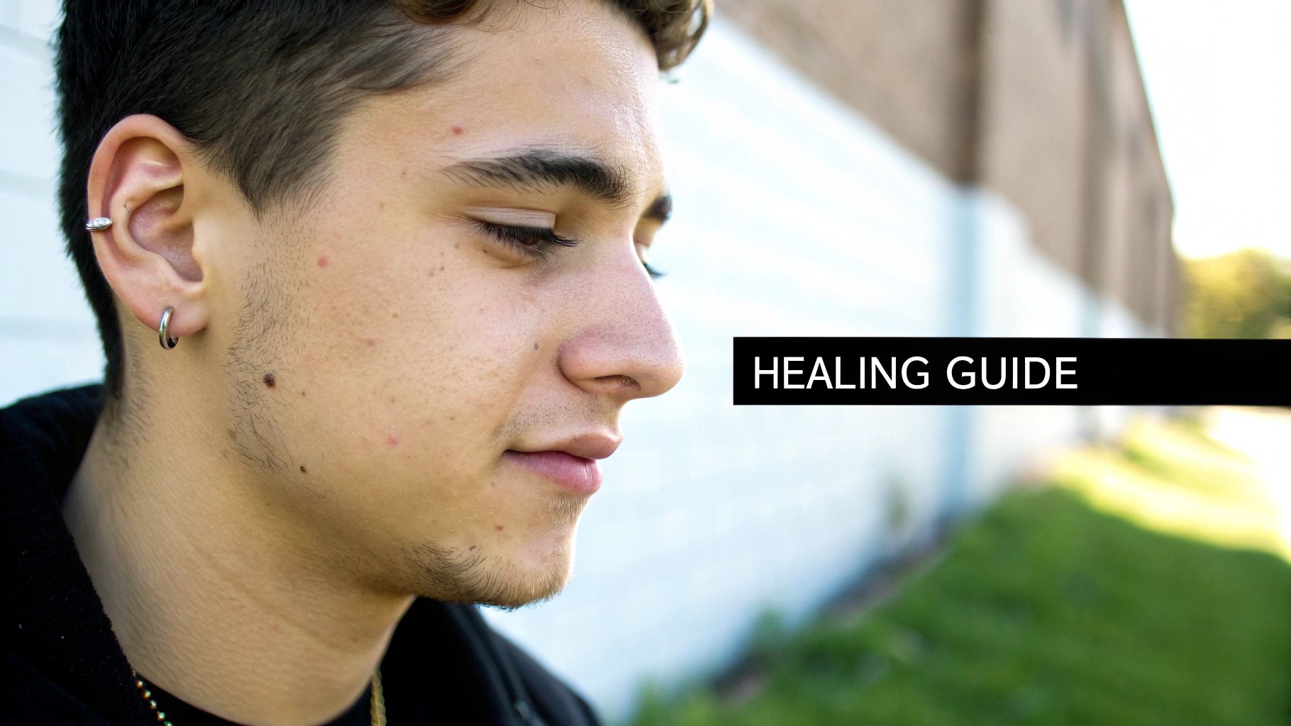 Close-up profile of a young man with two silver ear piercings, looking down, with 'HEALING GUIDE' text.