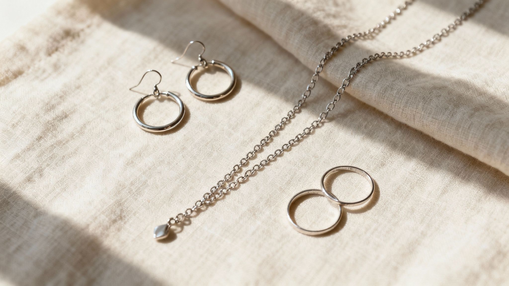 A collection of silver hoop earrings, a necklace, and rings on a light fabric.