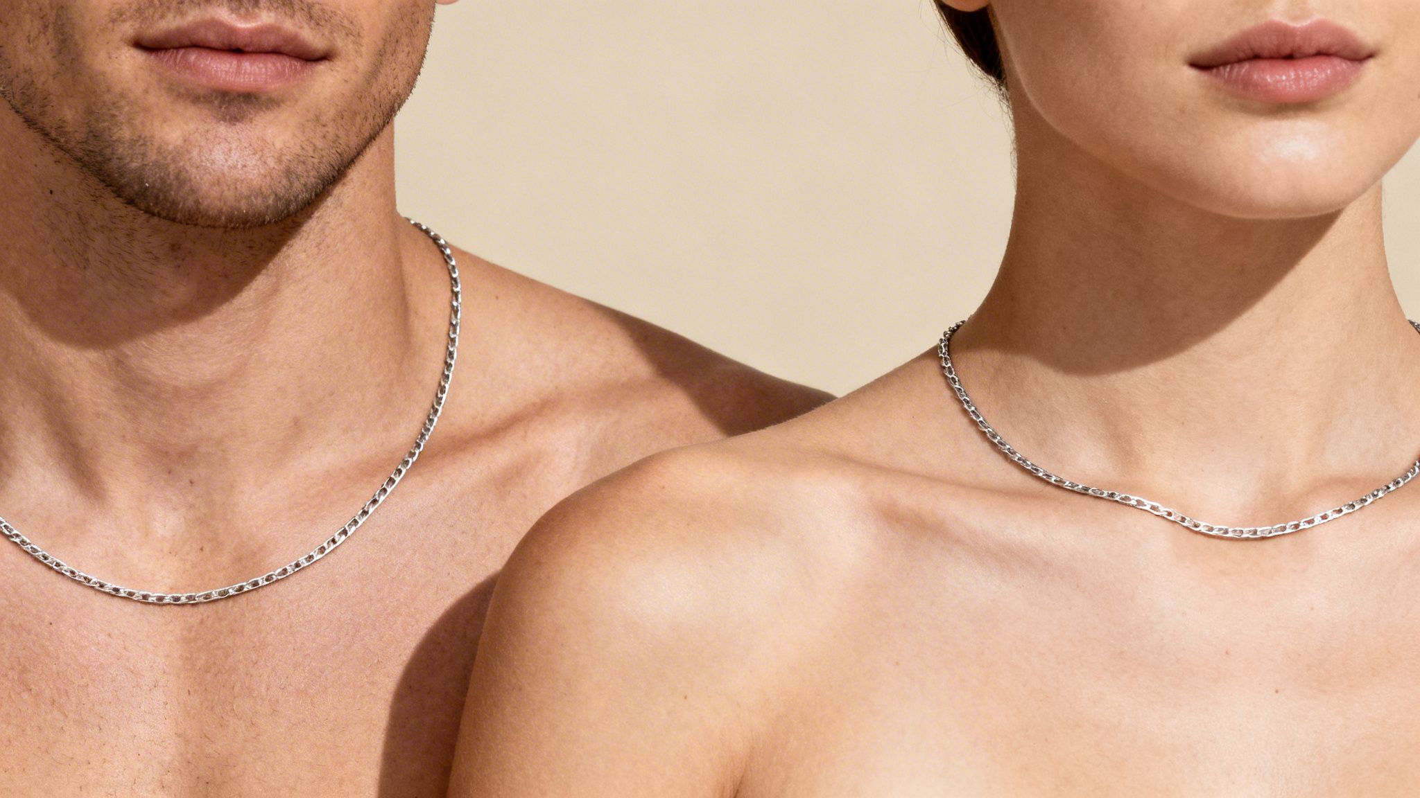 Close-up of a man and a woman wearing matching thin silver chain necklaces on their bare chests.
