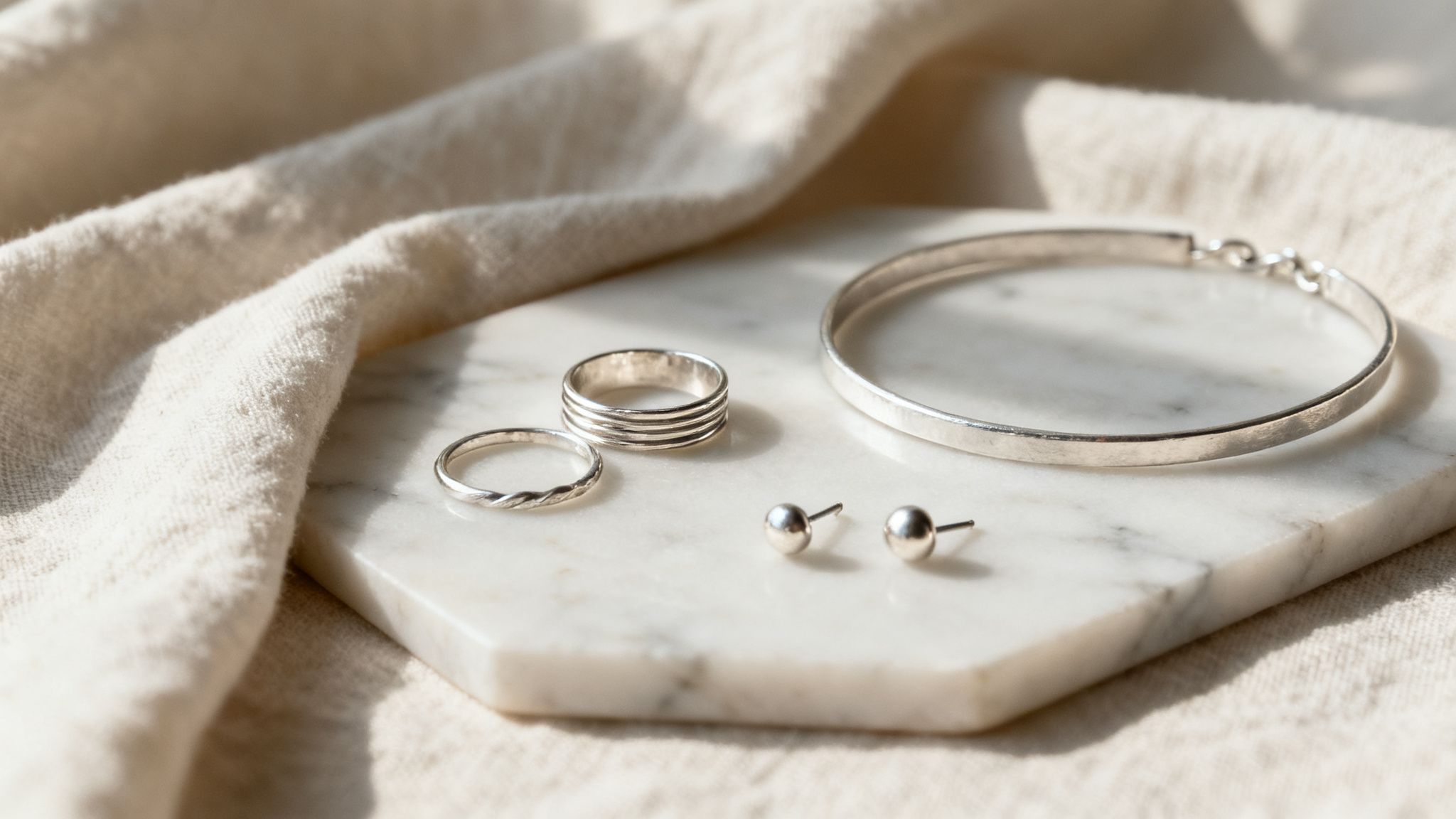 A collection of silver rings, stud earrings, and a bangle bracelet on a marble slab.