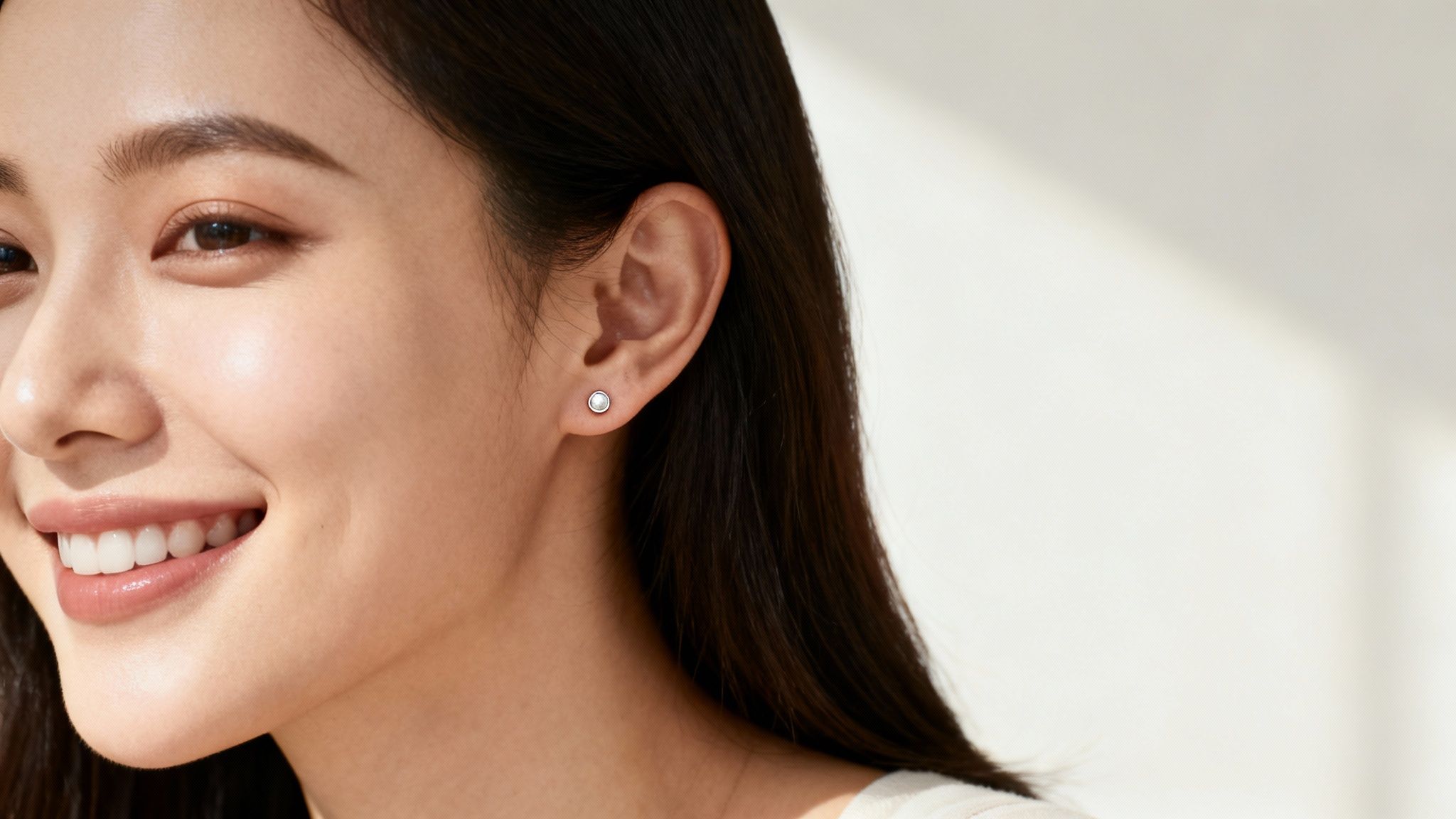 Close-up of a smiling woman wearing a single white stud earring on her ear.