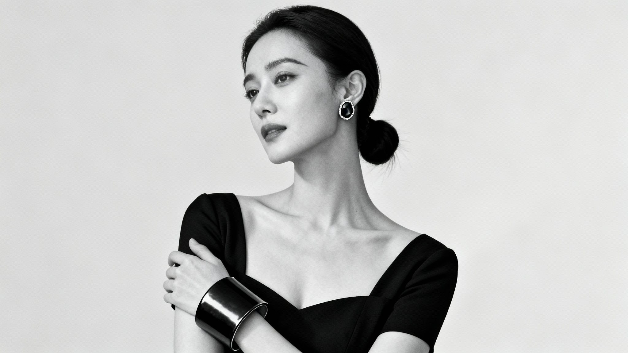 Чорно-білий портрет жінки з елегантною зачіскою, сережкою та браслетом, що дивиться убік.
