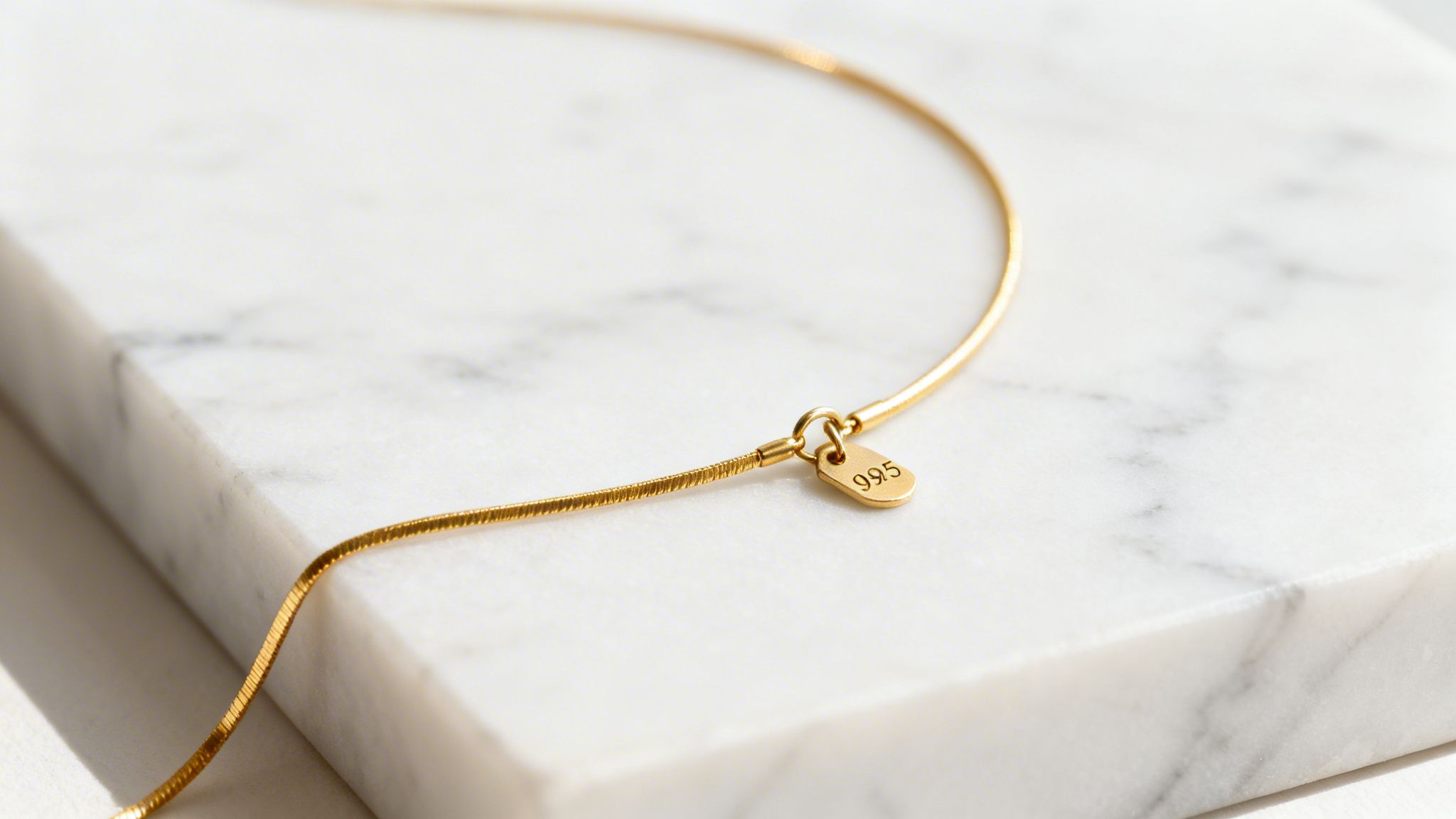 A shimmering gold snake chain necklace with a "995" tag rests on a white marble surface.