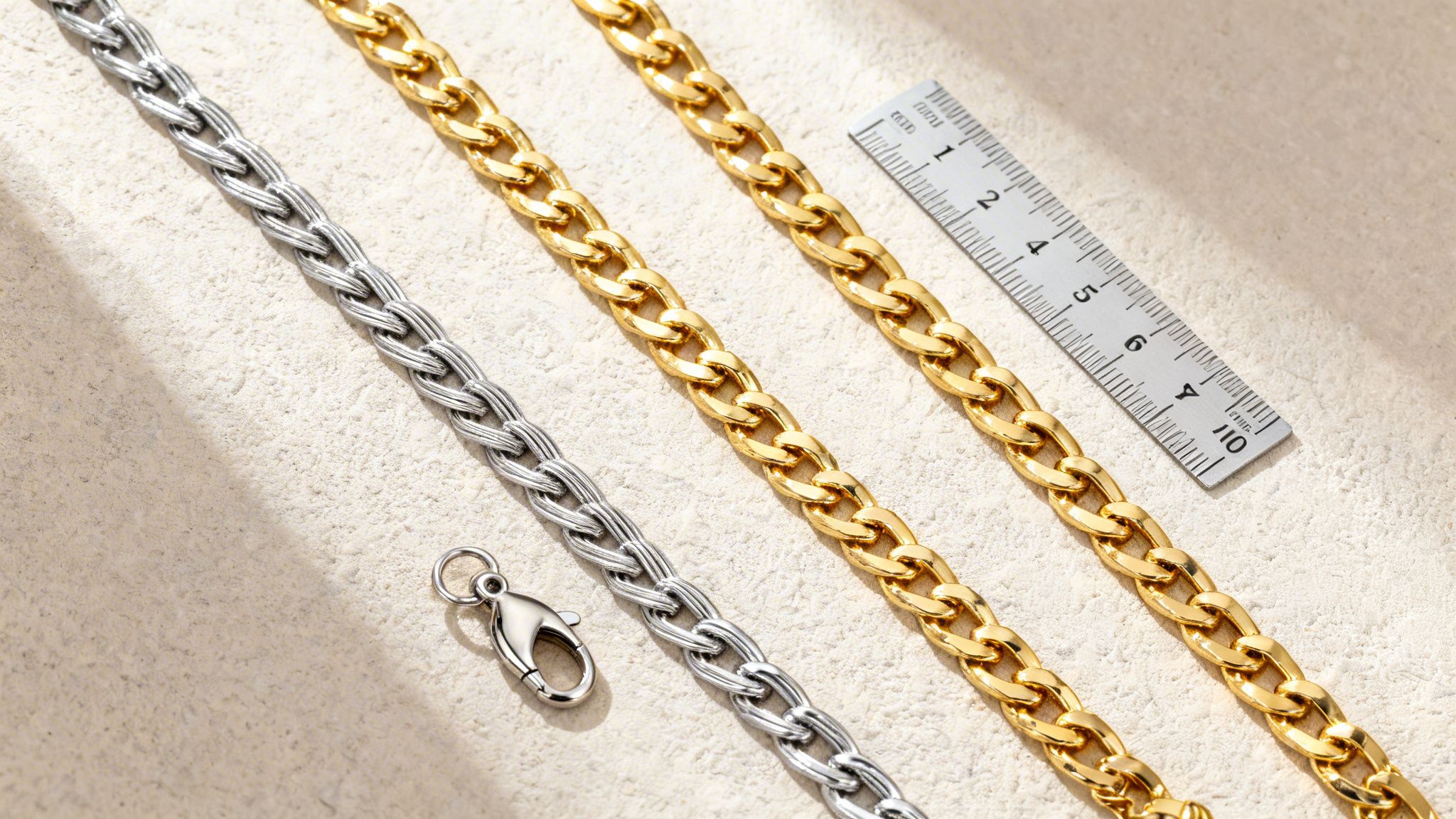 Three metal chains, one silver and two gold, with a ruler and lobster clasp on a textured surface.