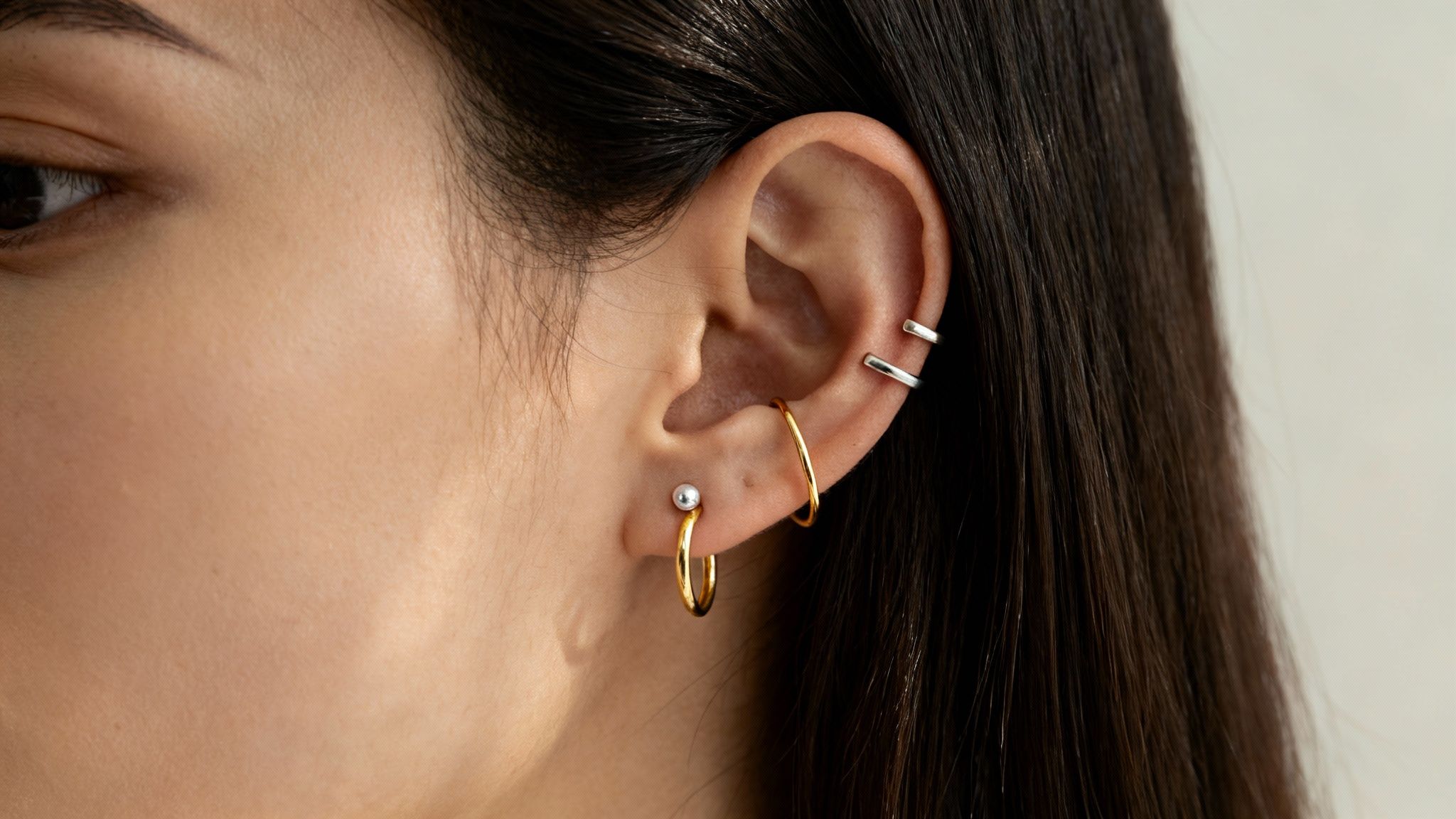 Close-up of a woman's ear featuring various gold hoop earrings and silver ear cuffs.