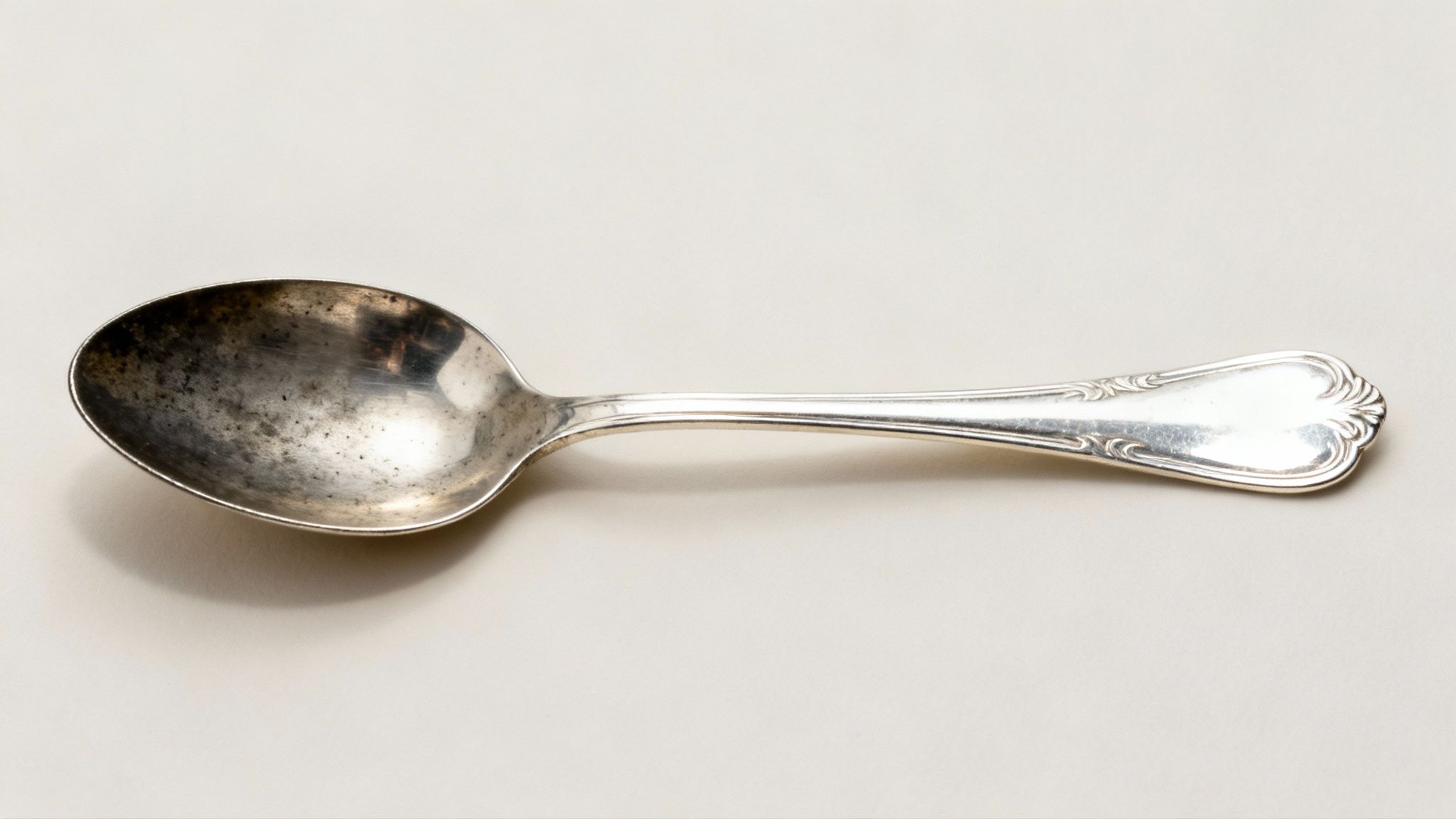 A tarnished silver spoon with an ornate handle rests on a light cream background.
