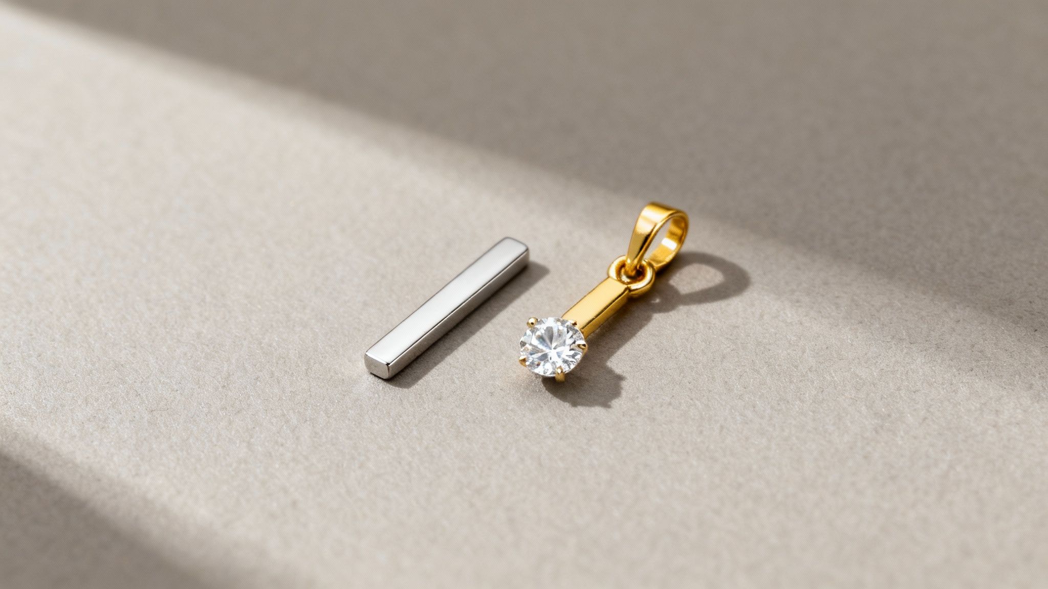 A gold pendant with a sparkling diamond and a silver bar on a textured light grey surface.