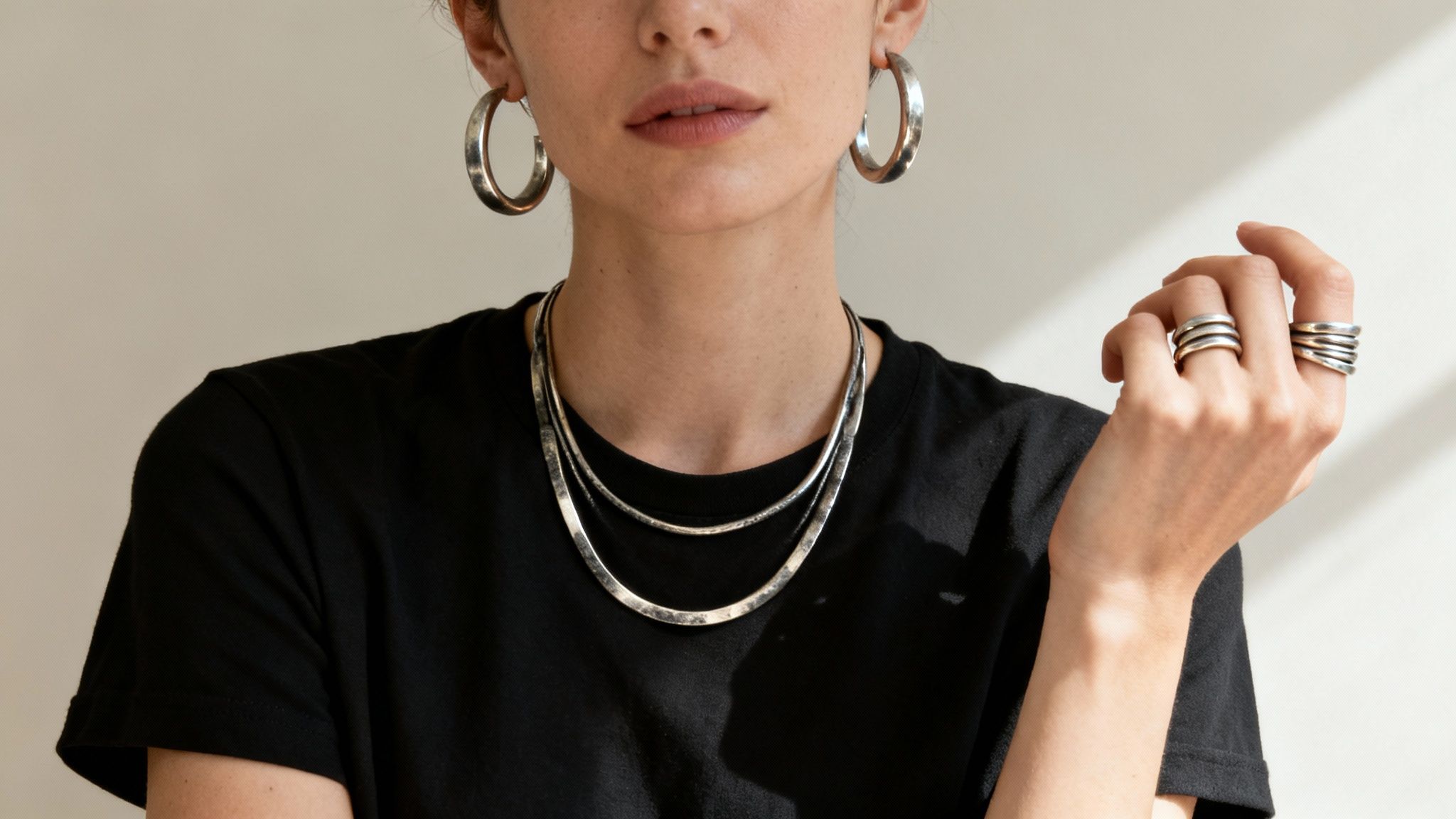 A person wearing multiple oxidised sterling silver jewelry pieces including hoop earrings, layered necklaces, and stacked rings.