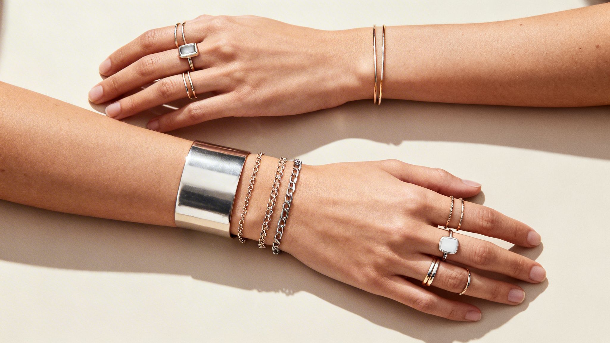 A person's hands and forearms adorned with various layered gold and silver rings, bracelets, and a cuff.