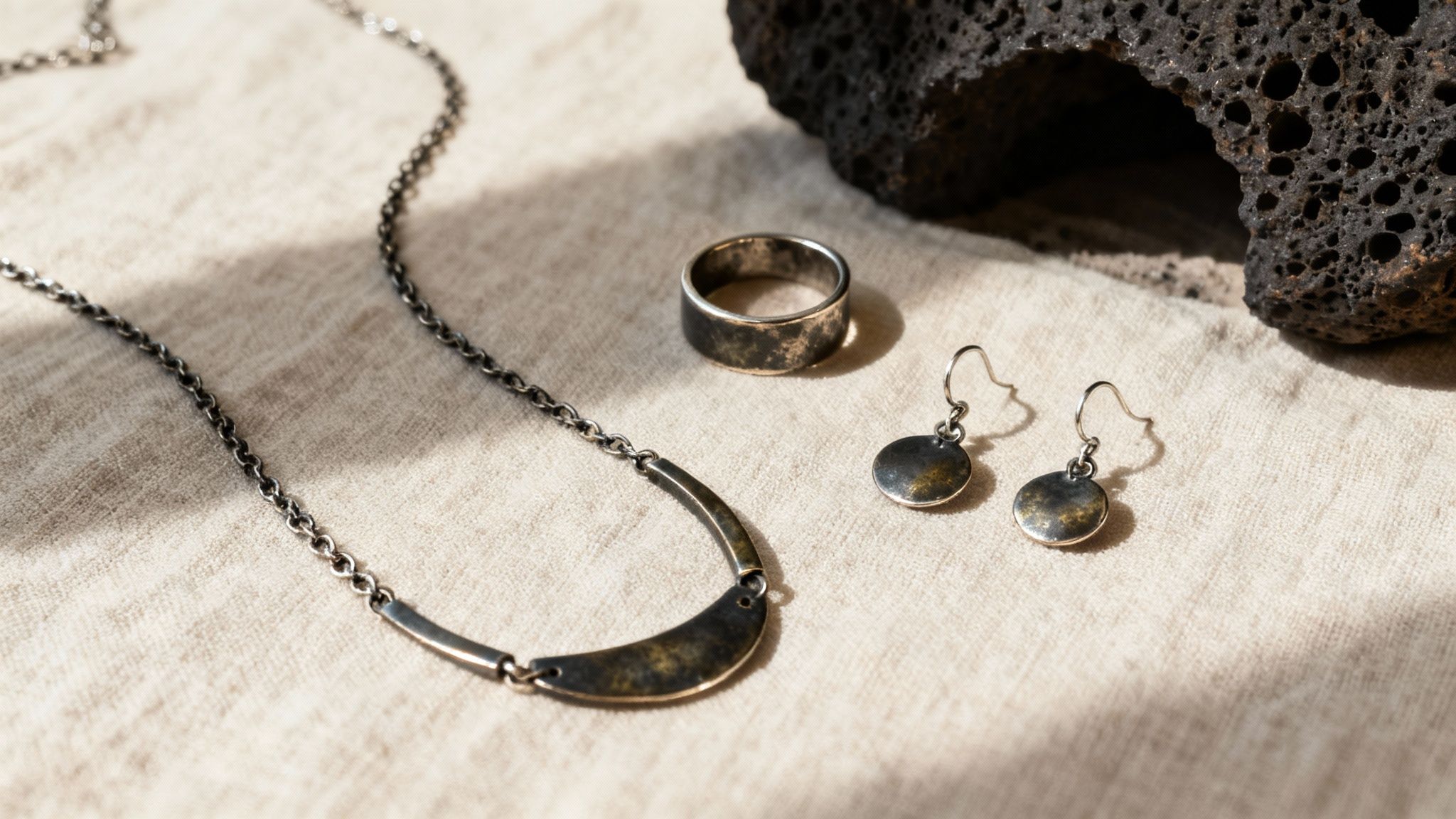 Oxidized sterling silver necklace, ring, and earrings displayed on light fabric next to a dark rock.