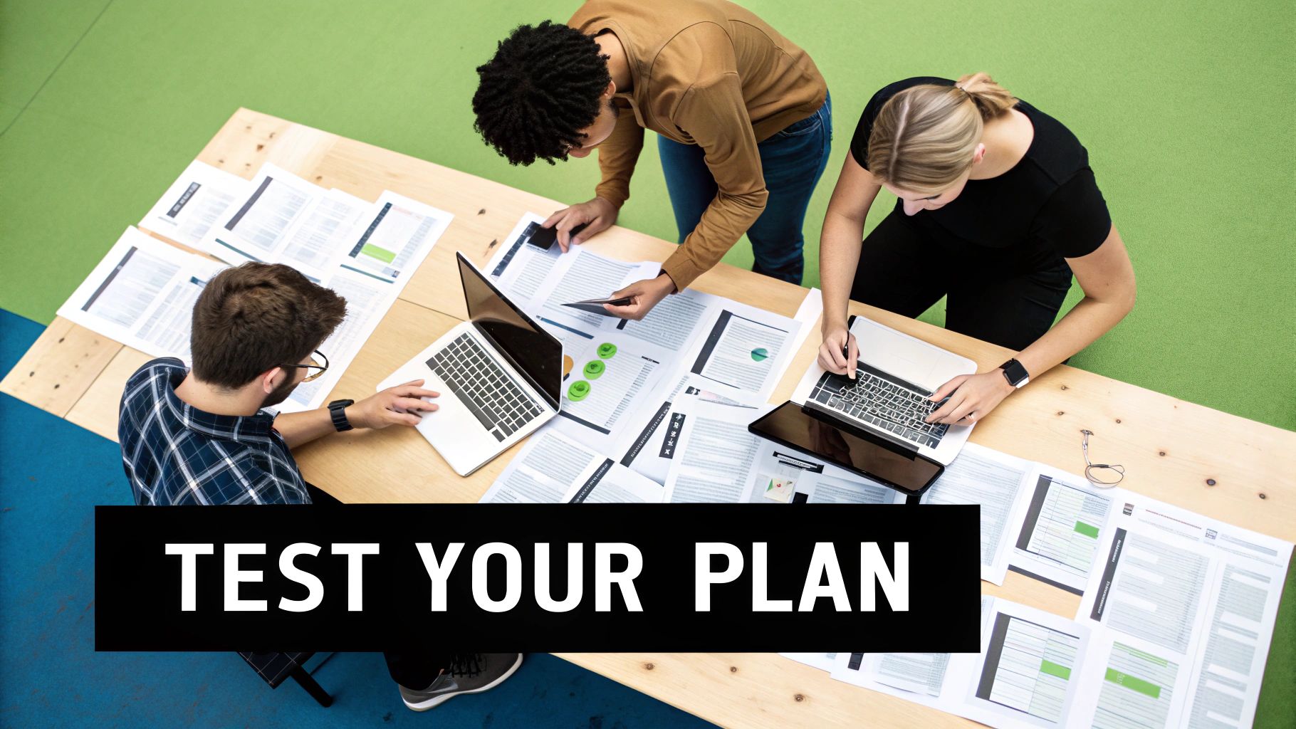 Overhead shot of three diverse professionals collaborating on laptops and papers at a wooden table.