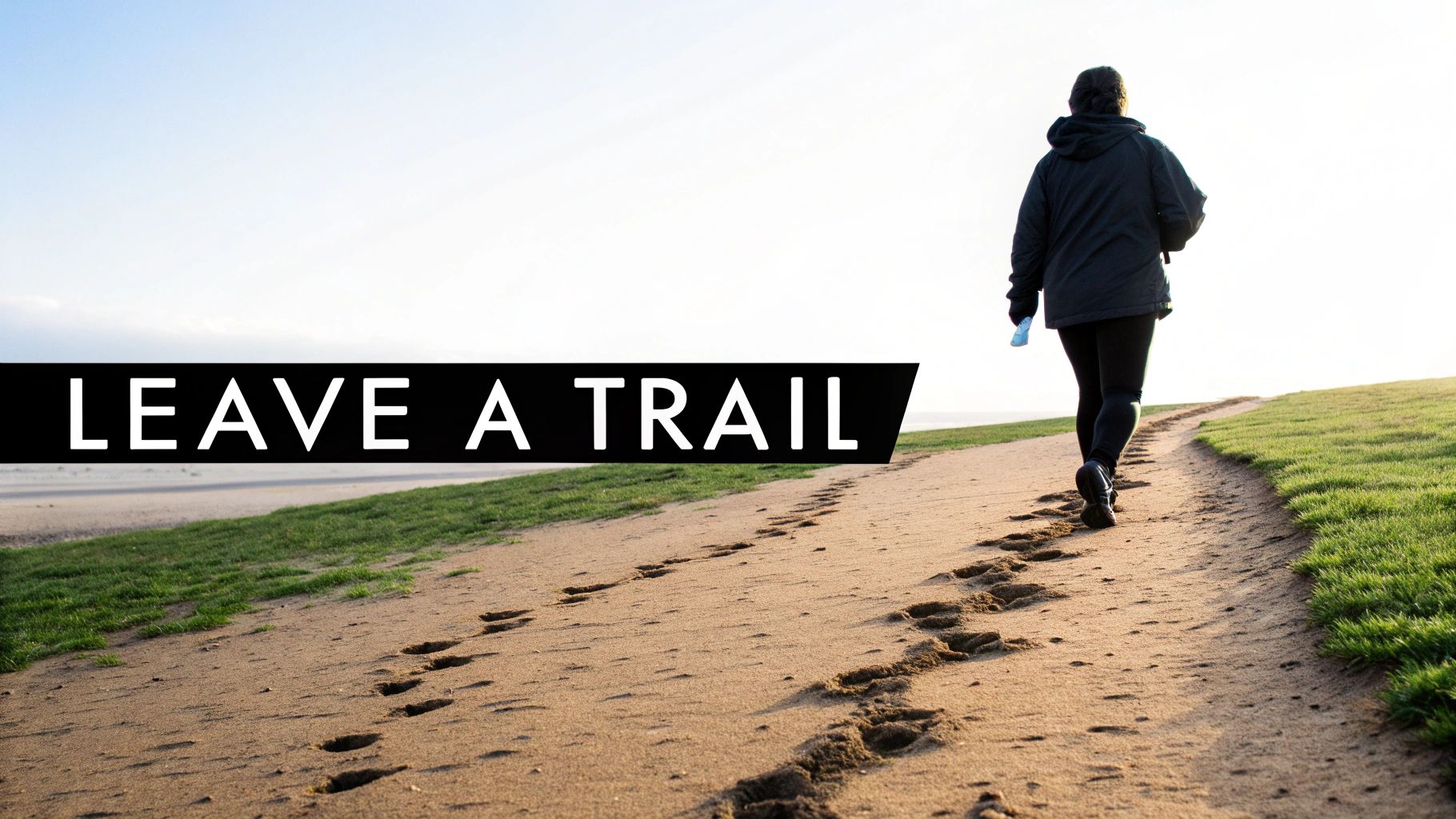 A person walks along a sandy path, leaving a visible trail of footprints behind them.
