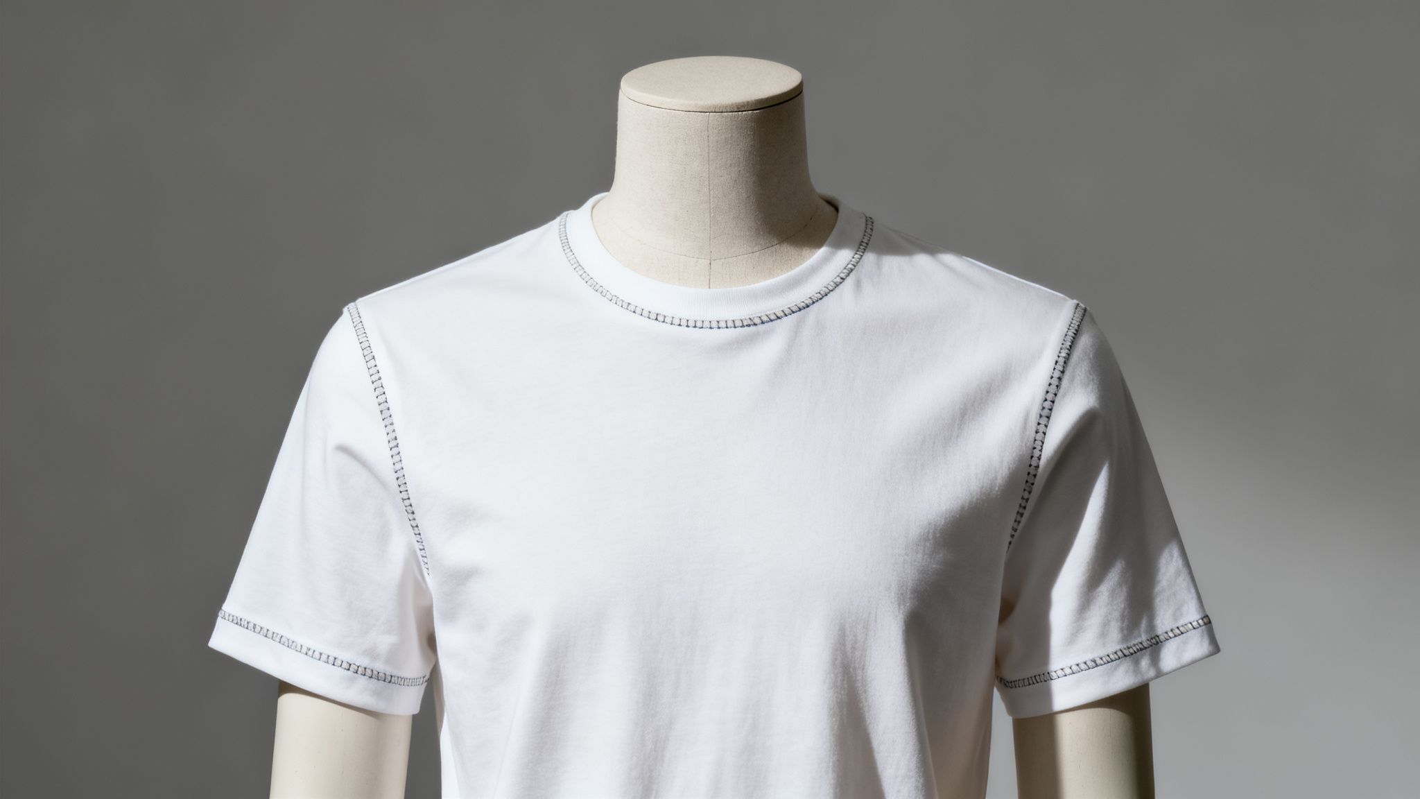 White t-shirt with visible dark contrast stitching on a mannequin against a grey background.
