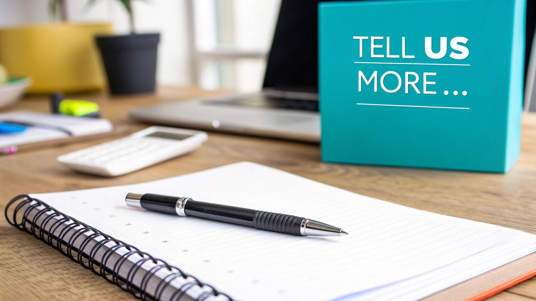 A desk with a notebook, pen, calculator, and a teal box displaying 'TELL US MORE...' text.
