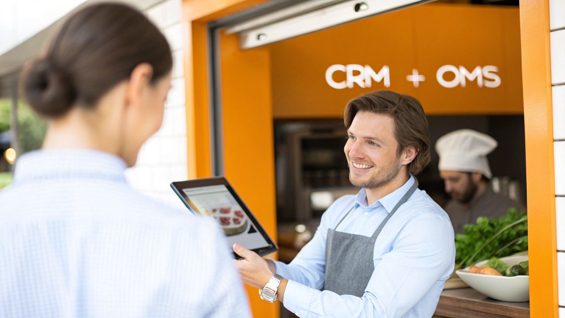Smiling man shows tablet menu to customer at food stand with 'CRM + OMS' sign.