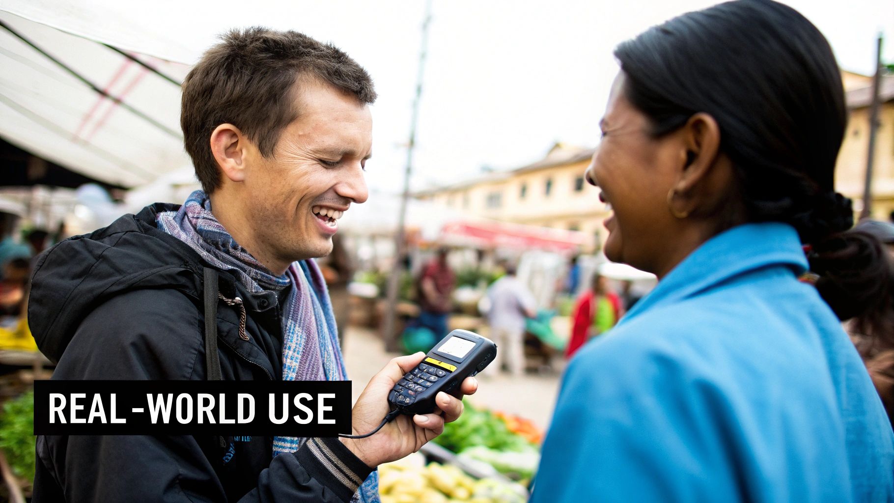Smiling man demonstrates a real-world use device to a woman at a vibrant market.