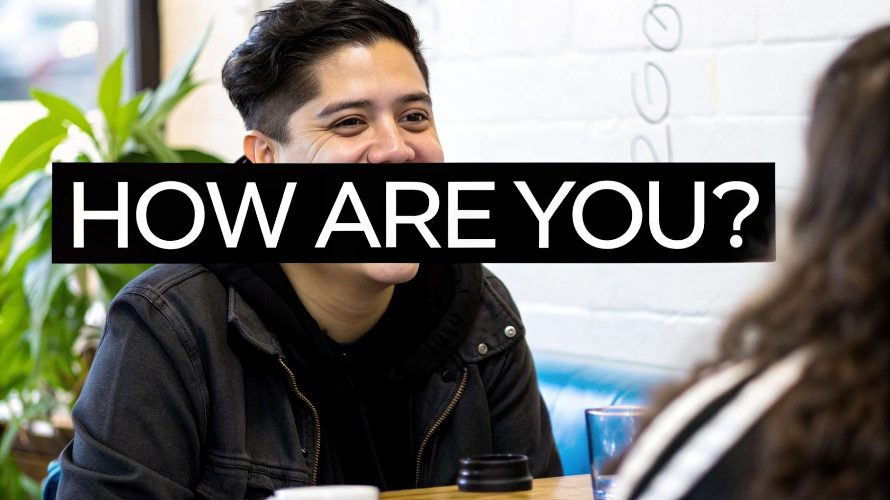 A smiling person in a black jacket sits at a table, with a 'HOW ARE YOU?' text overlay.