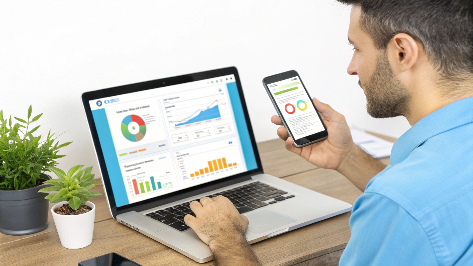 גבר עובד מול מחשב נייד ומסך סמארטפון, שניהם מציגים גרפים ונתונים עסקיים על שולחן עץ.