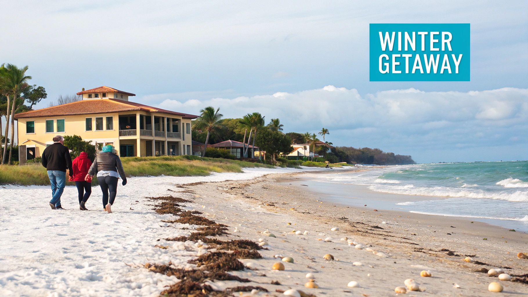 People enjoy a winter getaway, walking on a sandy beach with a large house and ocean waves.