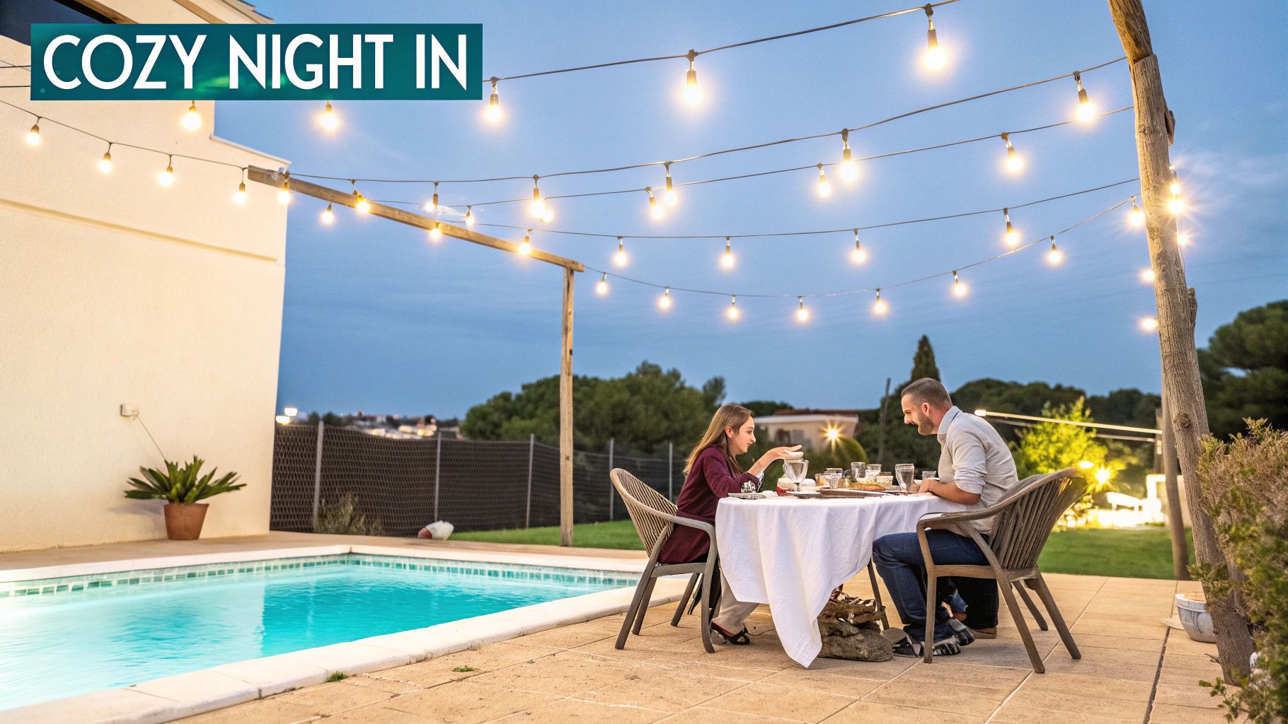 A couple enjoys a romantic outdoor dinner by a pool, illuminated by string lights.