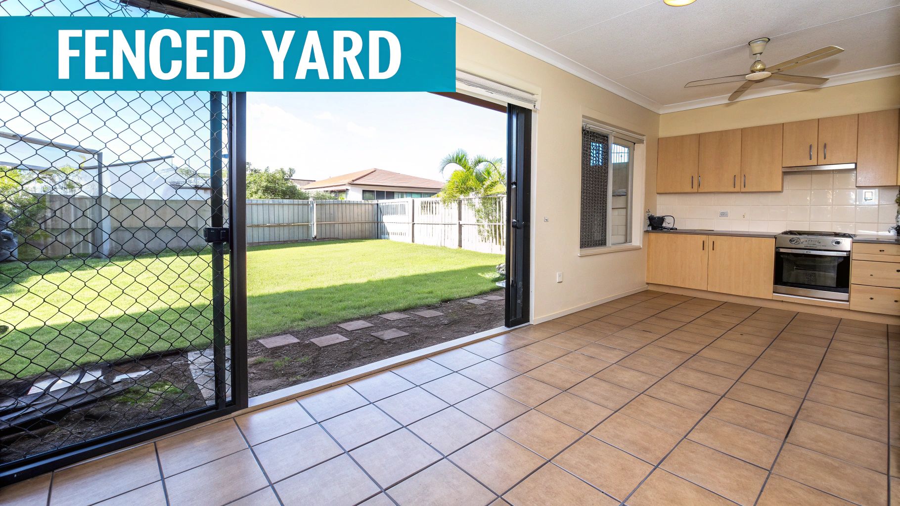 A combined kitchen and living area with tiled floors opens to a bright, fenced grassy backyard.