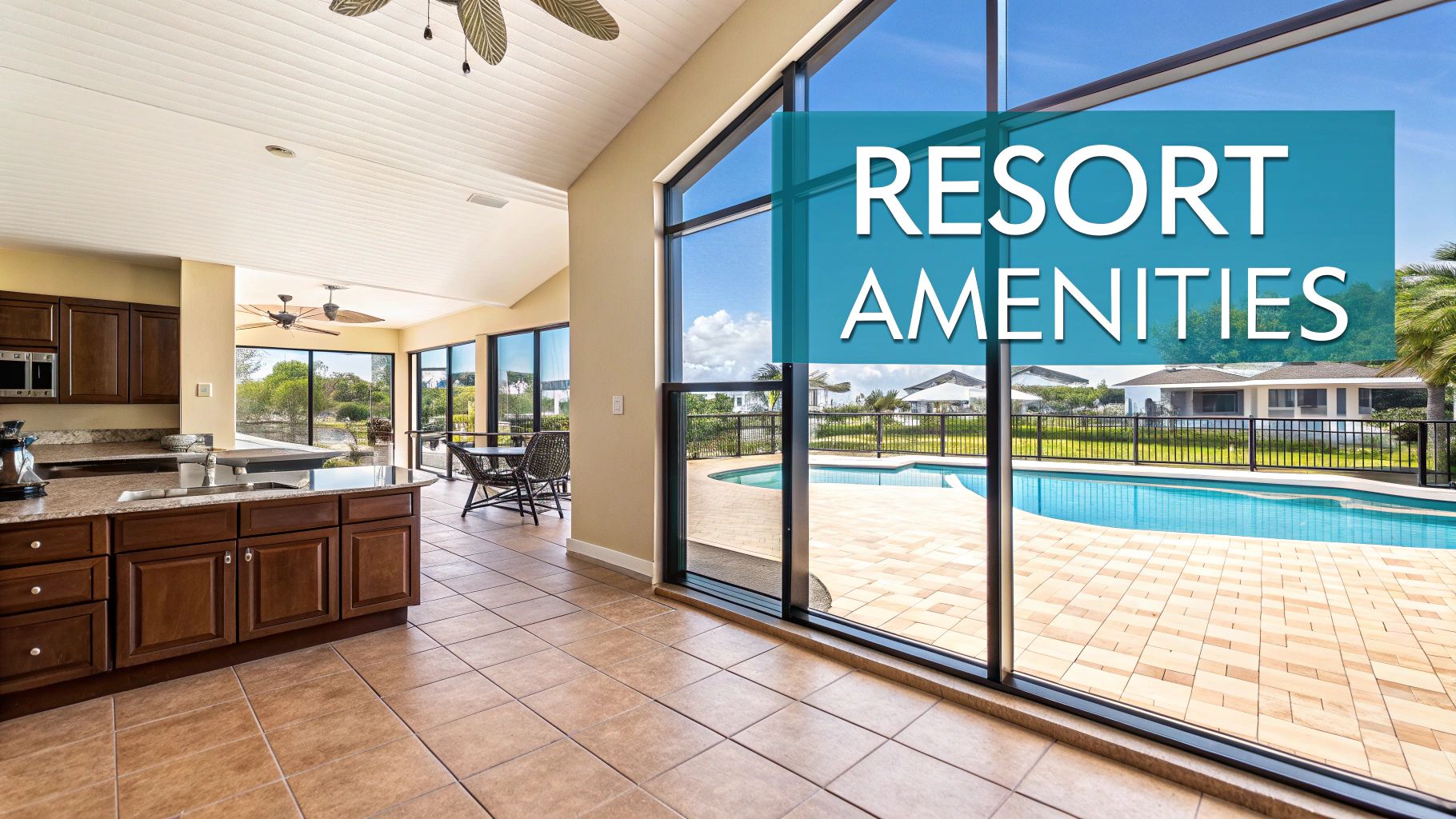 An indoor kitchen and living area with large windows opening to a resort pool and houses.