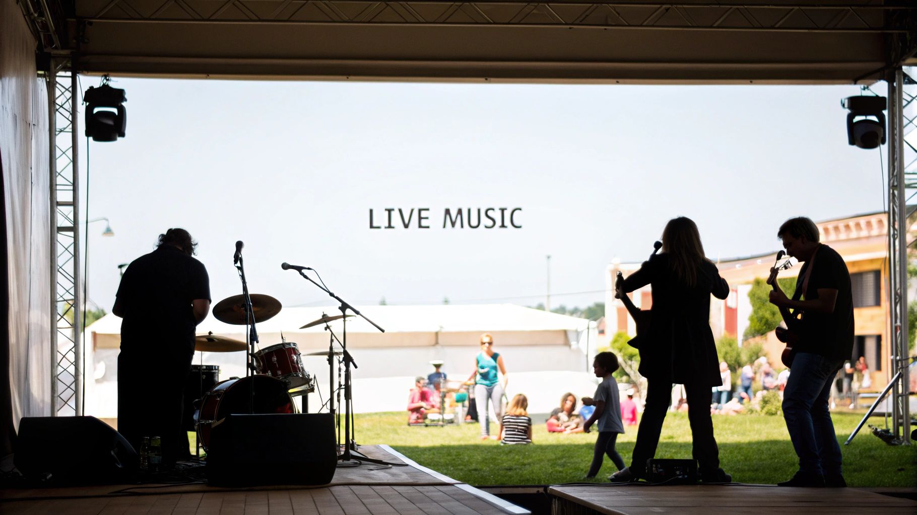 Silhouetted band performs live music on an outdoor stage for a relaxed audience on a sunny day.