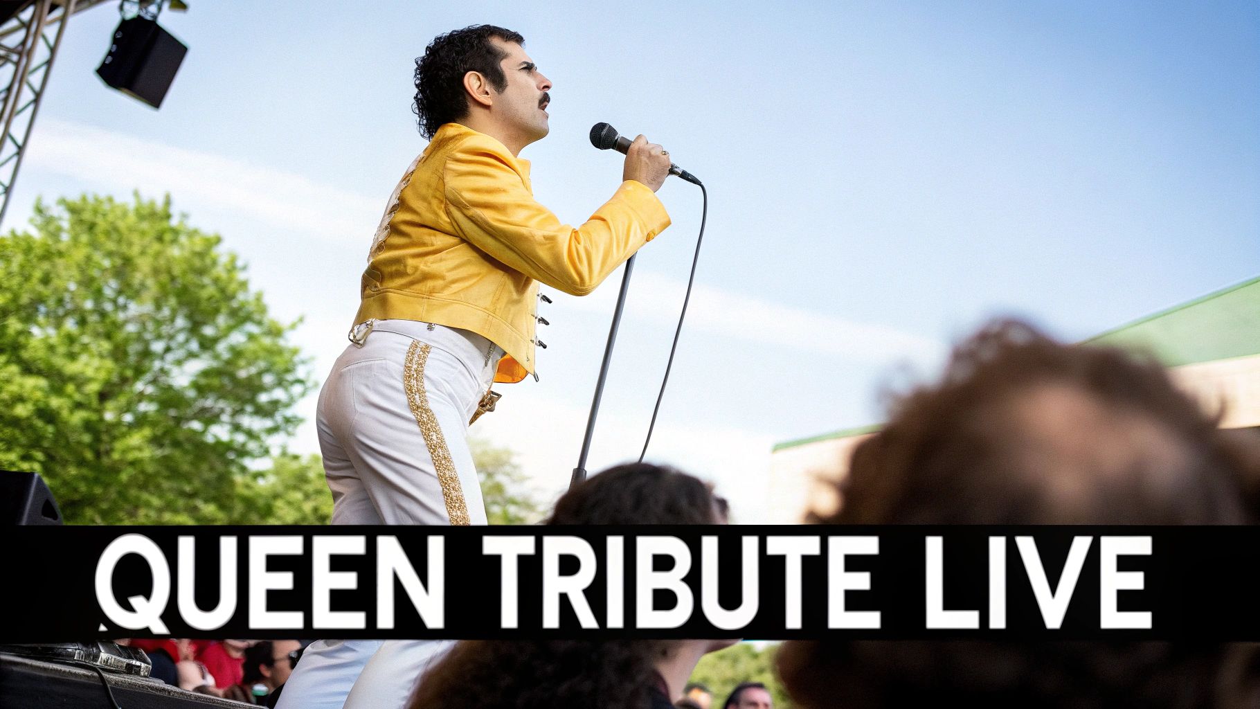 A performer in a yellow jacket and mustache sings into a microphone during a Queen tribute concert.