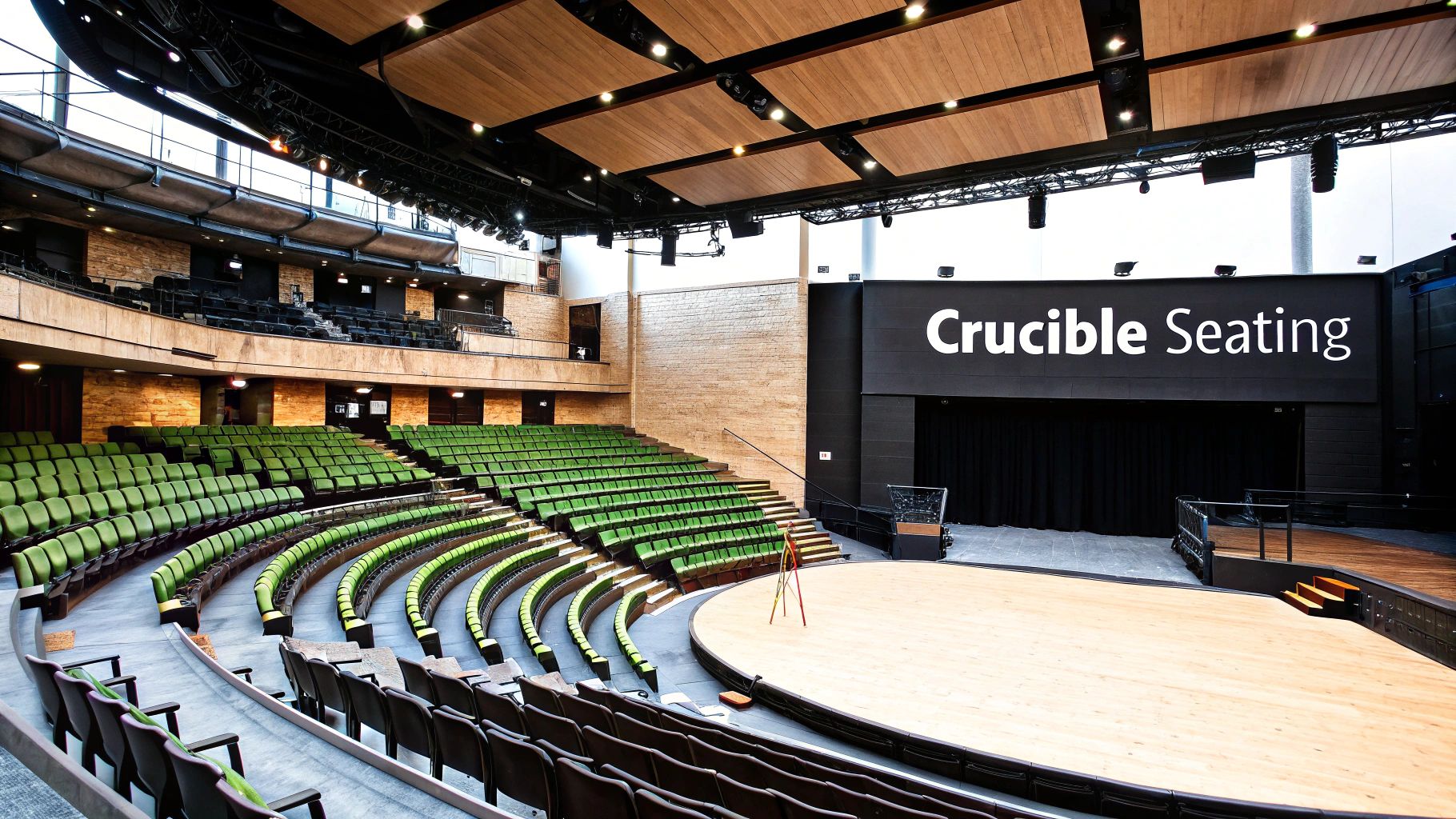 An empty, modern theatre auditorium with multiple levels of green seating and a stage displaying "Crucible Seating".