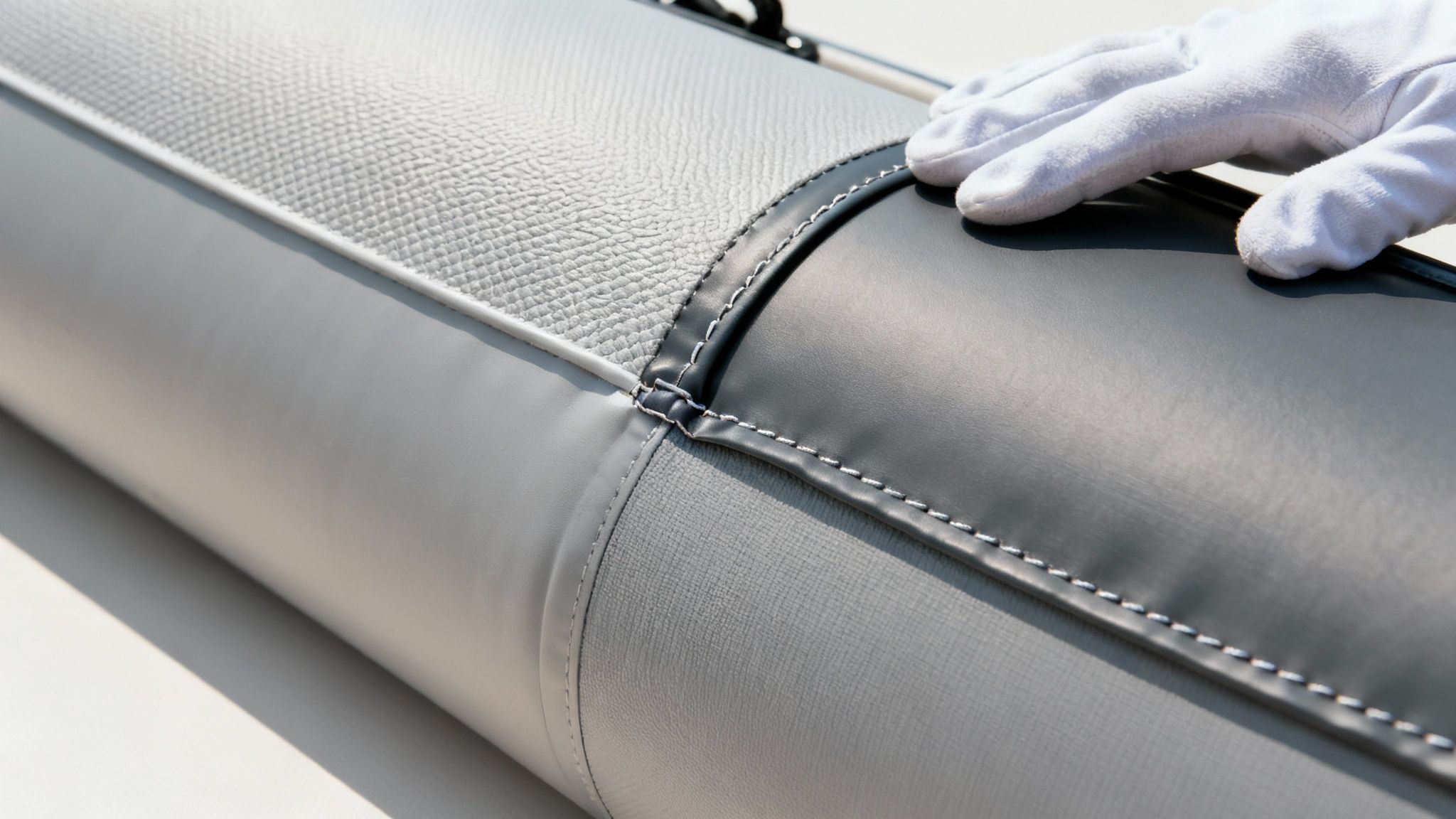 A gloved hand inspects the textured and smooth grey fabric of an inflatable boat.