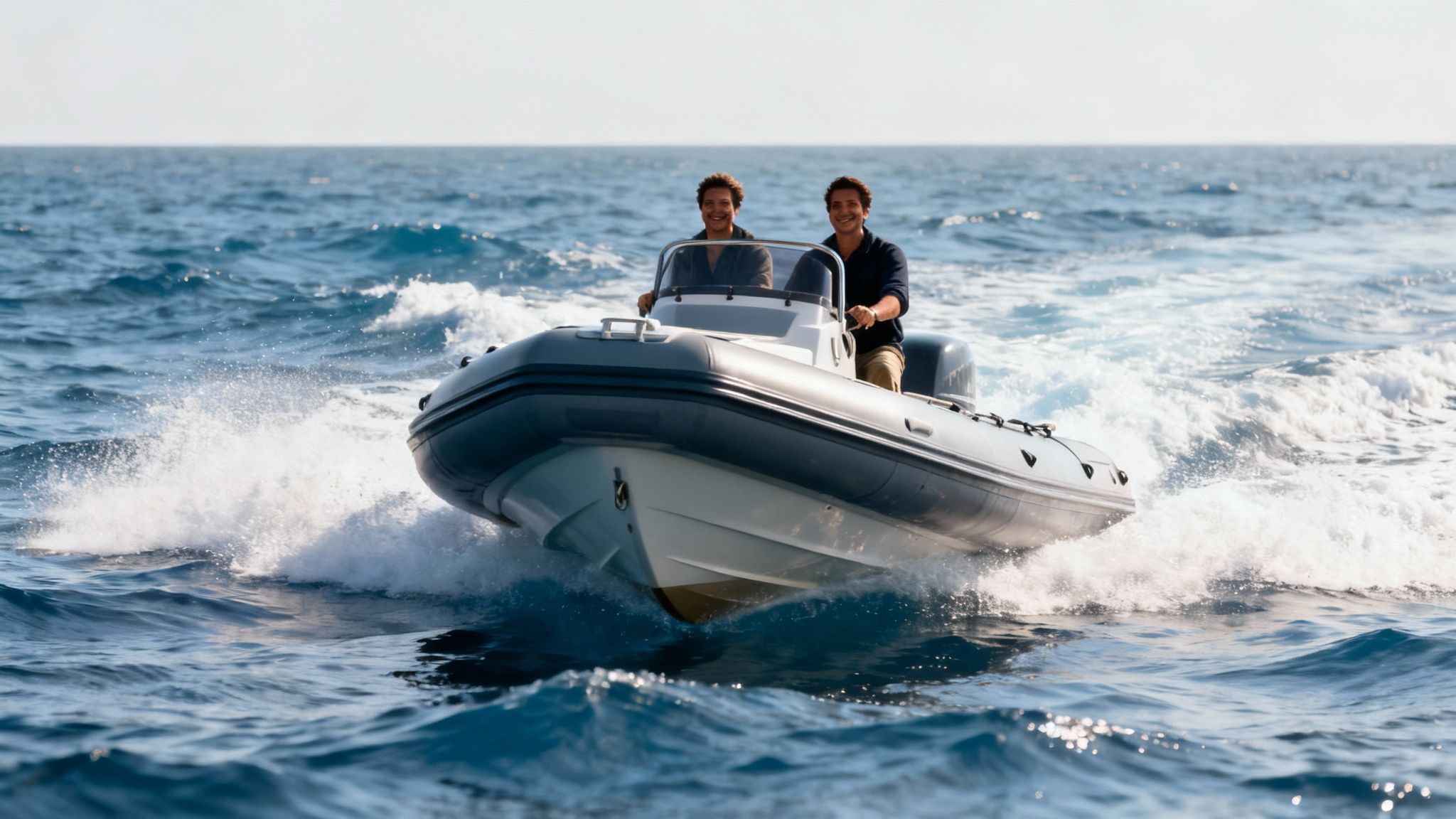 Two smiling men drive a rigid inflatable boat fast across blue ocean water.