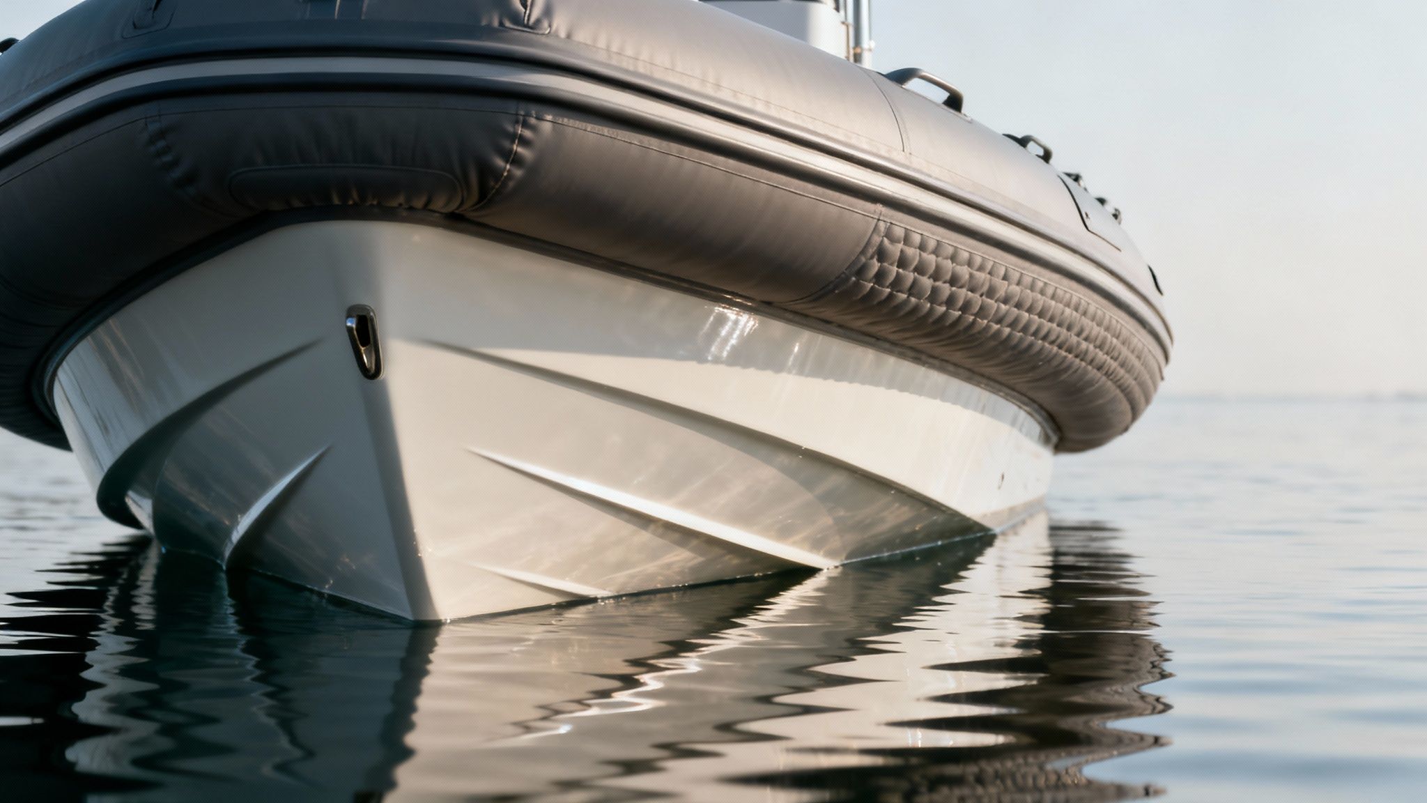 Close-up of the bow of a modern rigid inflatable boat (RIB) floating on still water with reflections.
