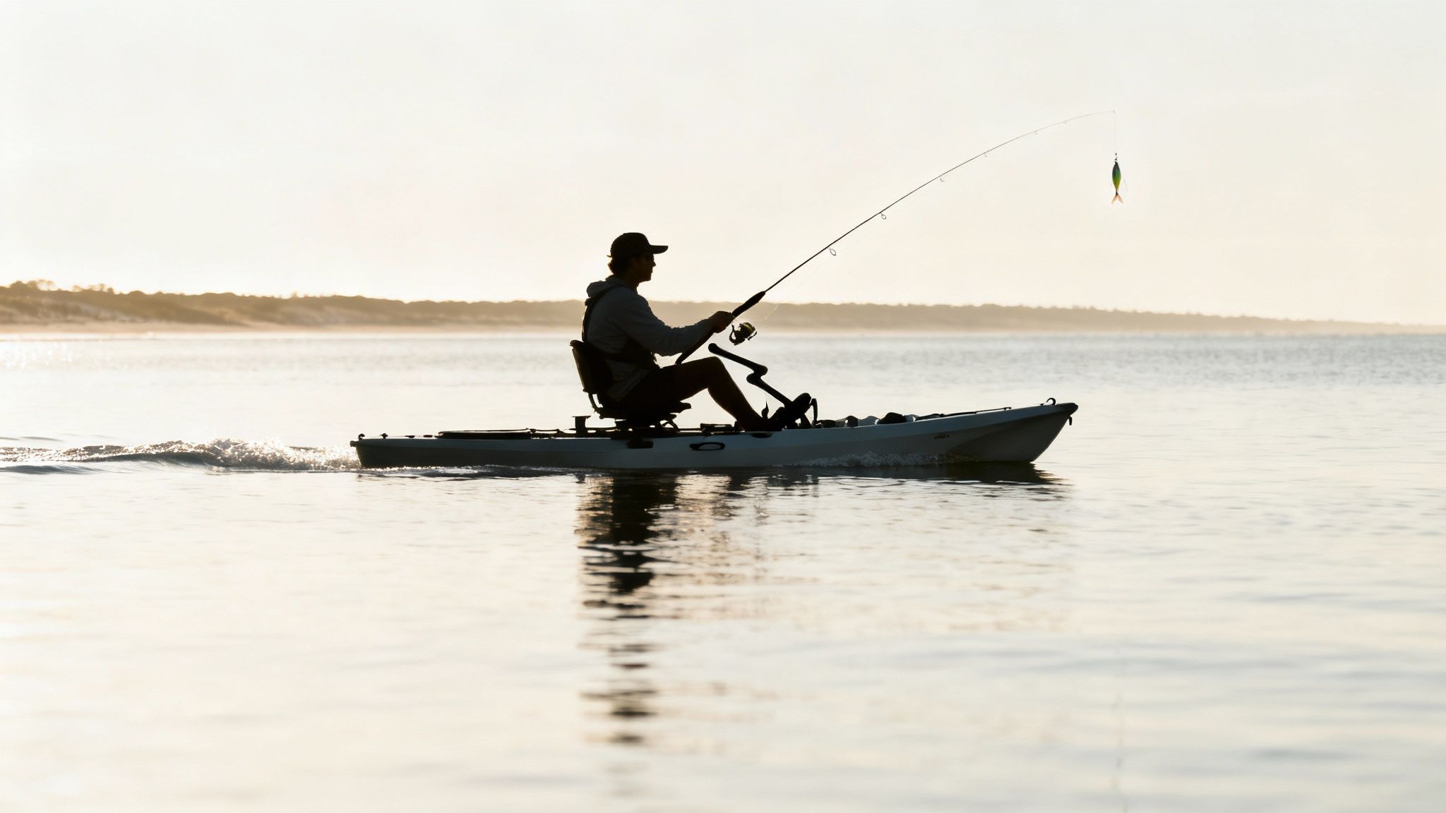 Silhouette of a man fishing from a pedal kayak on calm water during sunrise.