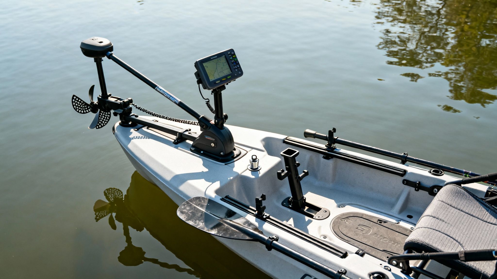 A white fishing kayak equipped with a bow-mounted trolling motor, fish finder, and paddle on calm water.