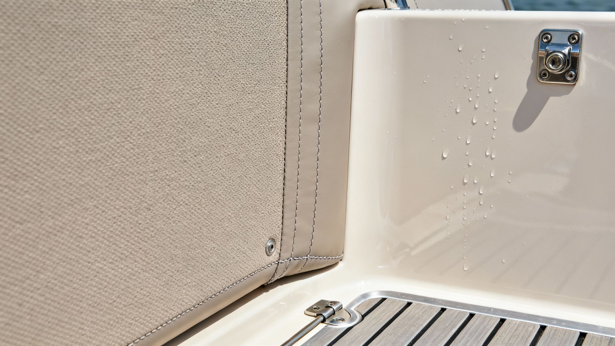 Detailed view of a boat's interior, showing beige fabric upholstery, a wet panel, and chrome hardware.