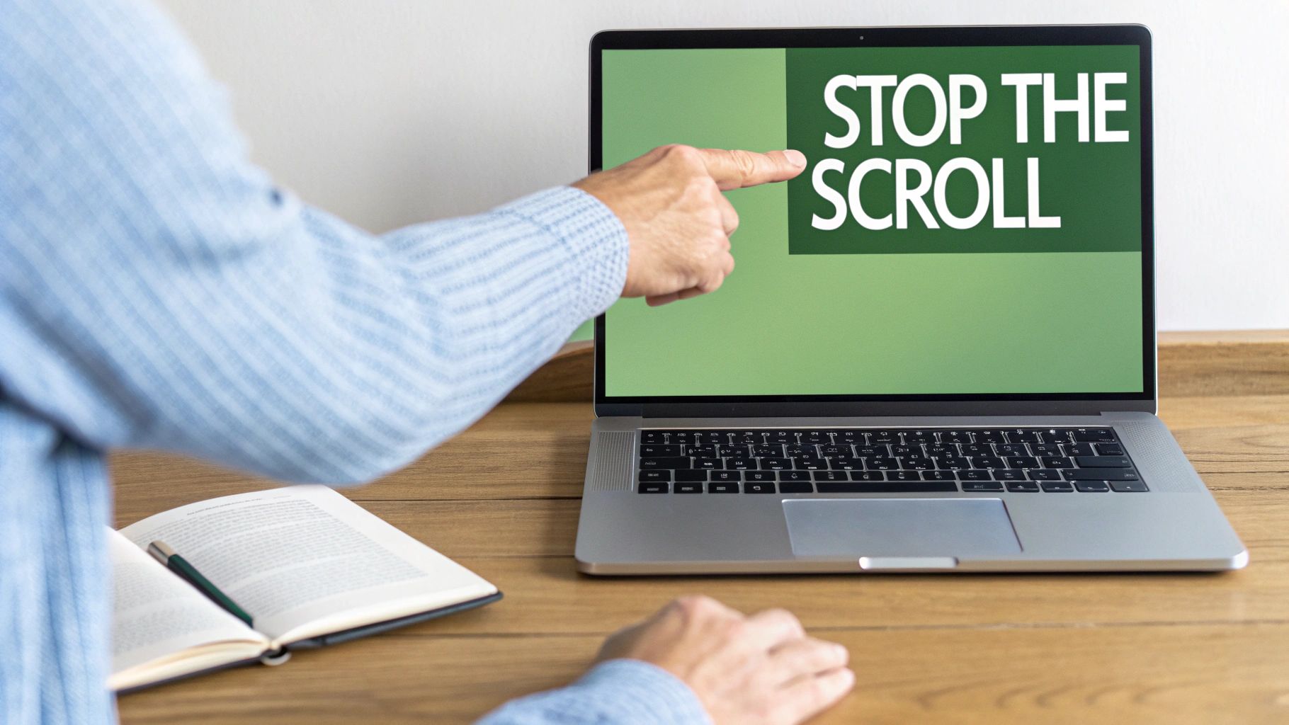 A person's hand points at a laptop screen displaying the text 'STOP THE SCROLL' on a green background, with an open book nearby.