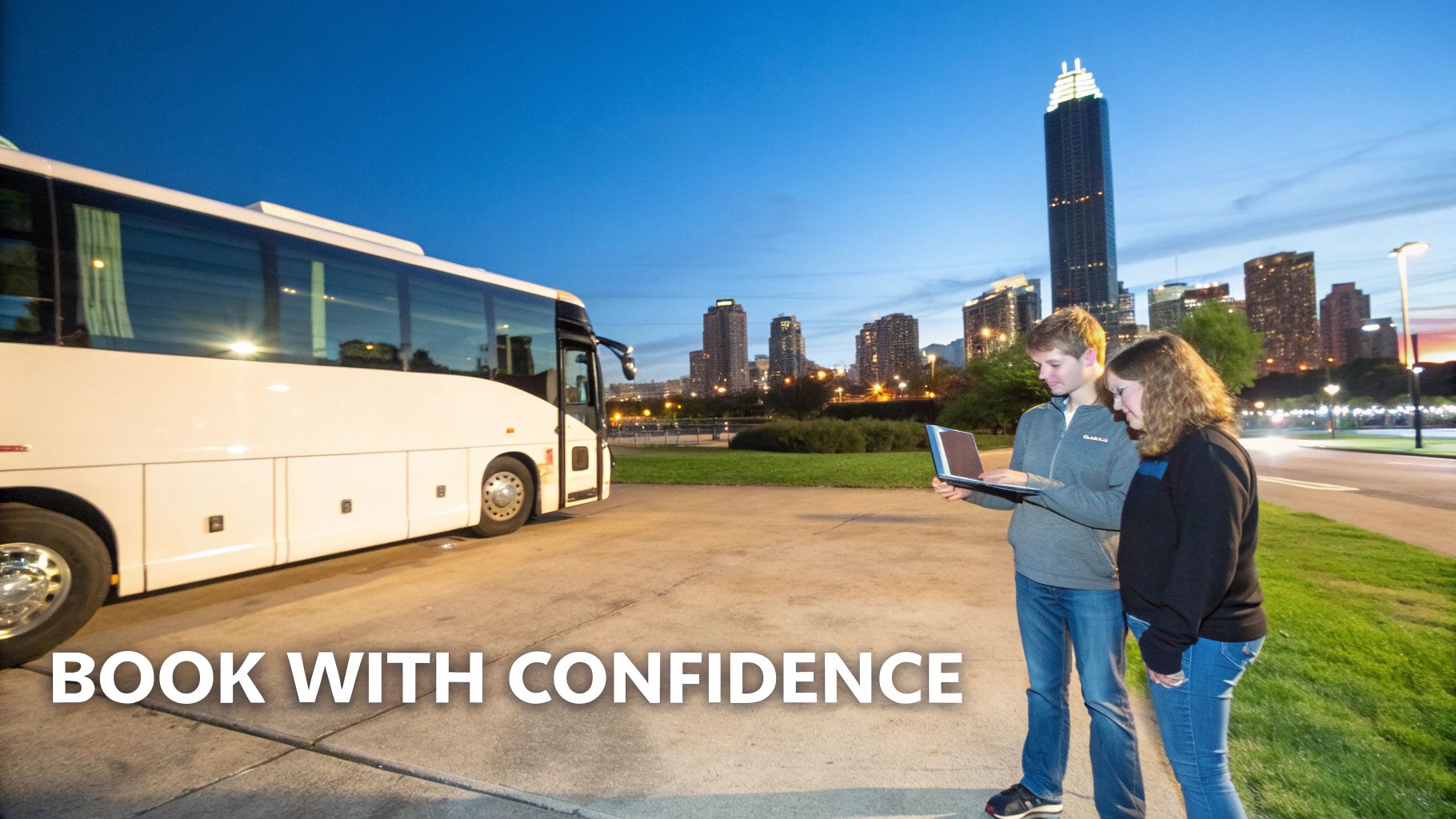 Two people look at a laptop near a white tour bus with a city skyline at dusk.