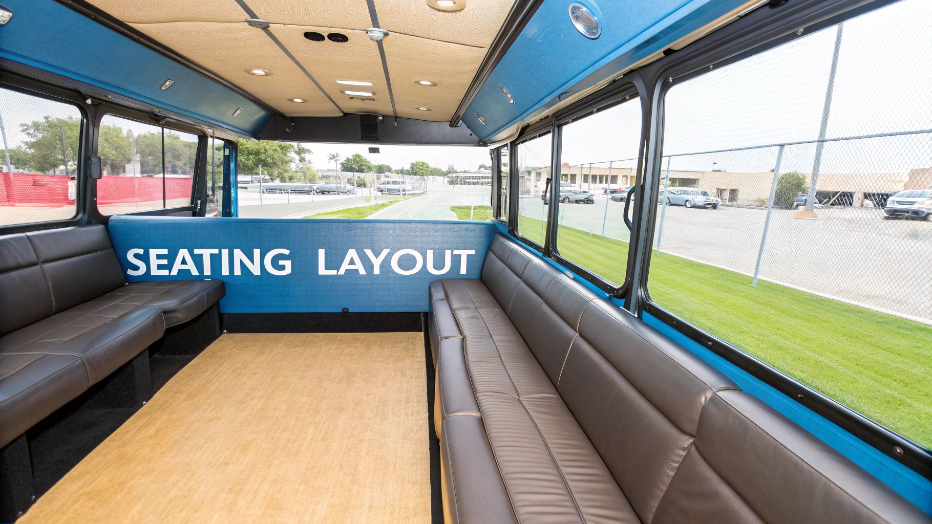 Interior view of a party bus showing brown leather bench seats, a blue wall, and windows.